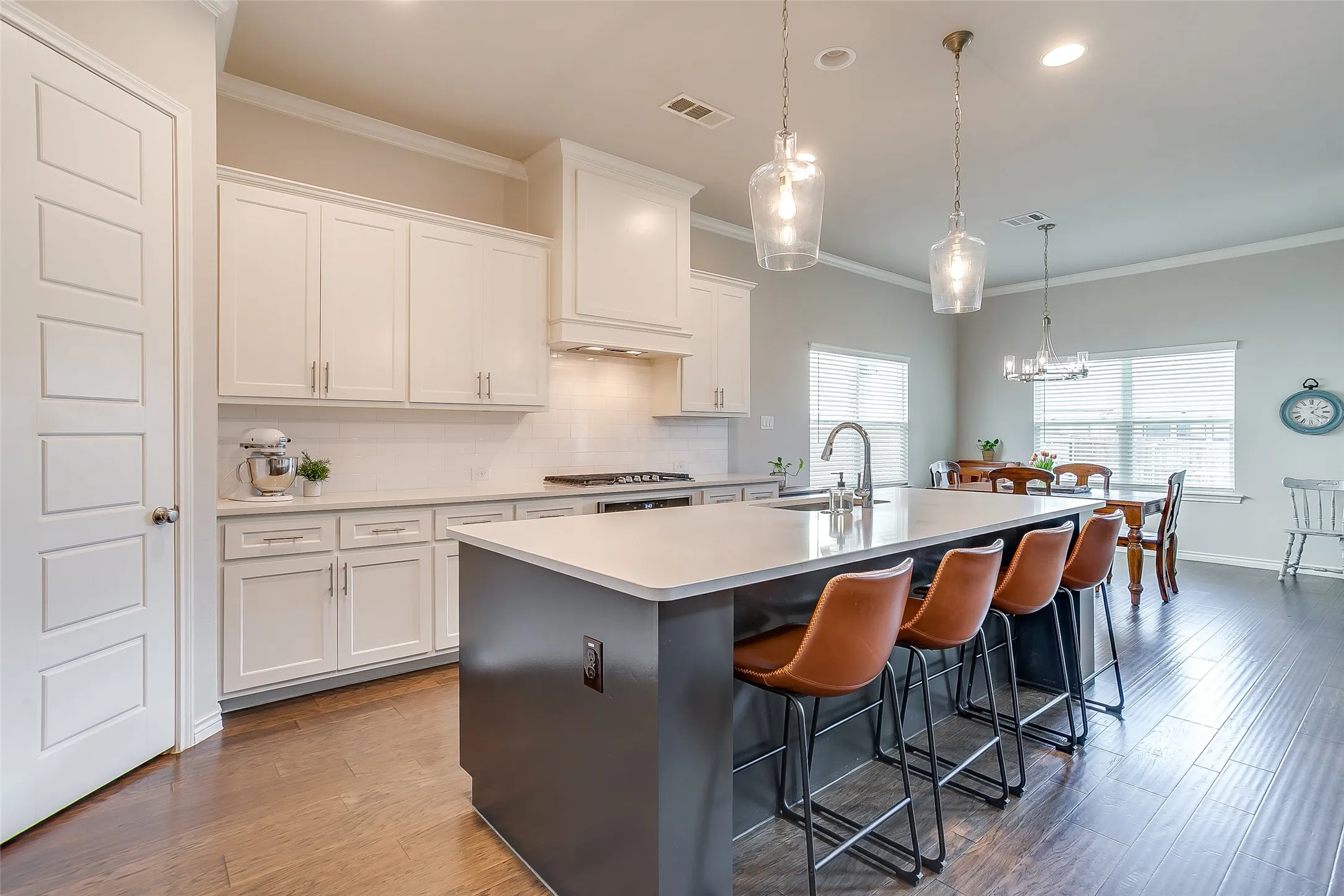 Spacious kitchen featuring an expansive island with seating, white shaker cabinetry, a white subway tile backsplash, and wood-finish flooring
