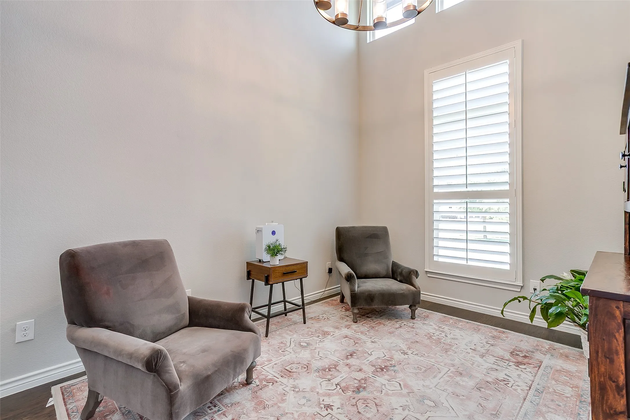 Room featuring dark wood-finish flooring, light-toned walls, and a tall window with white plantation shutters