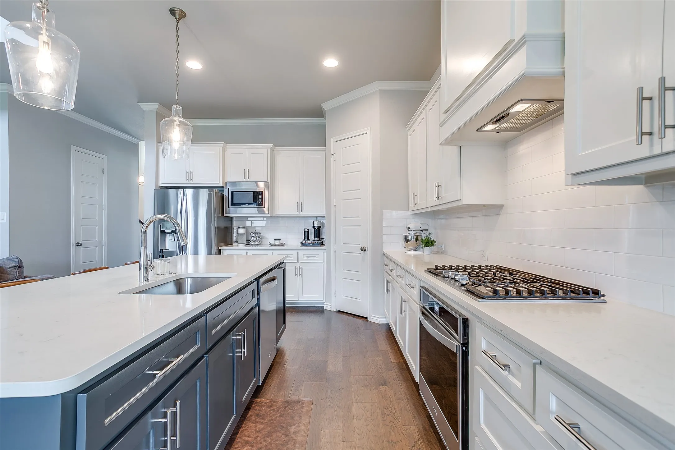 Kitchen featuring white shaker cabinetry, stainless steel appliances, a center island with a sink, white countertops, and wood-finish flooring