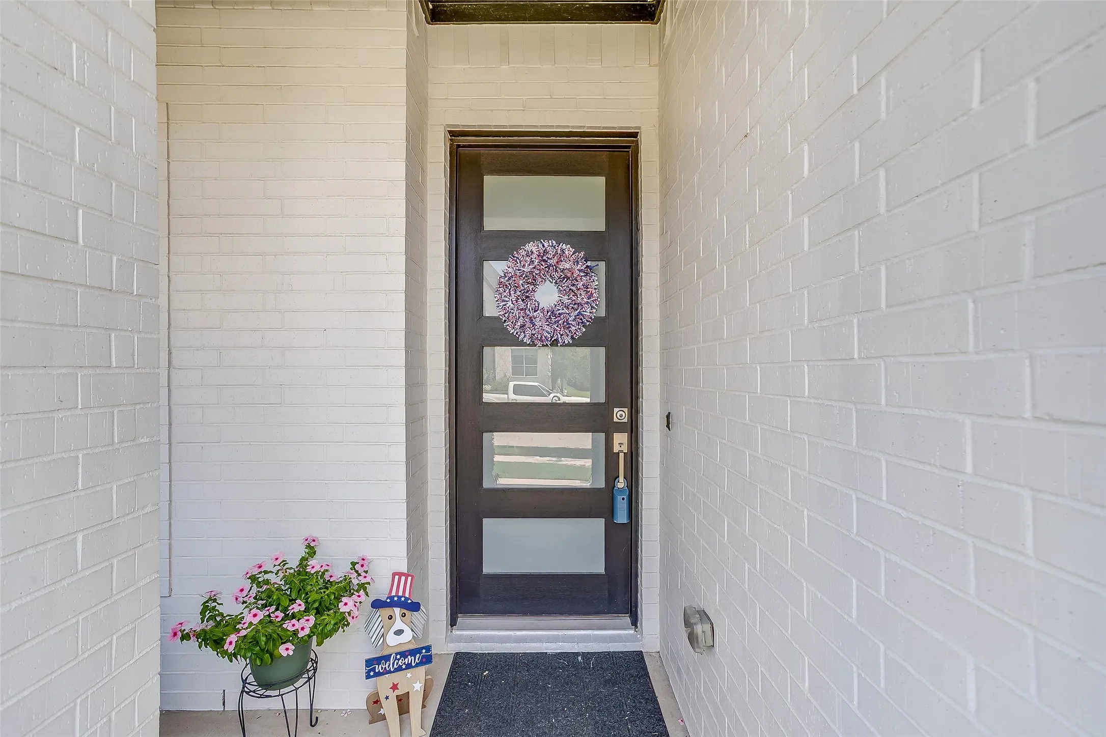 Modern dark-finish entry door with frosted rectangular glass inserts, complemented by painted brick exterior walls and a dark-finish door frame