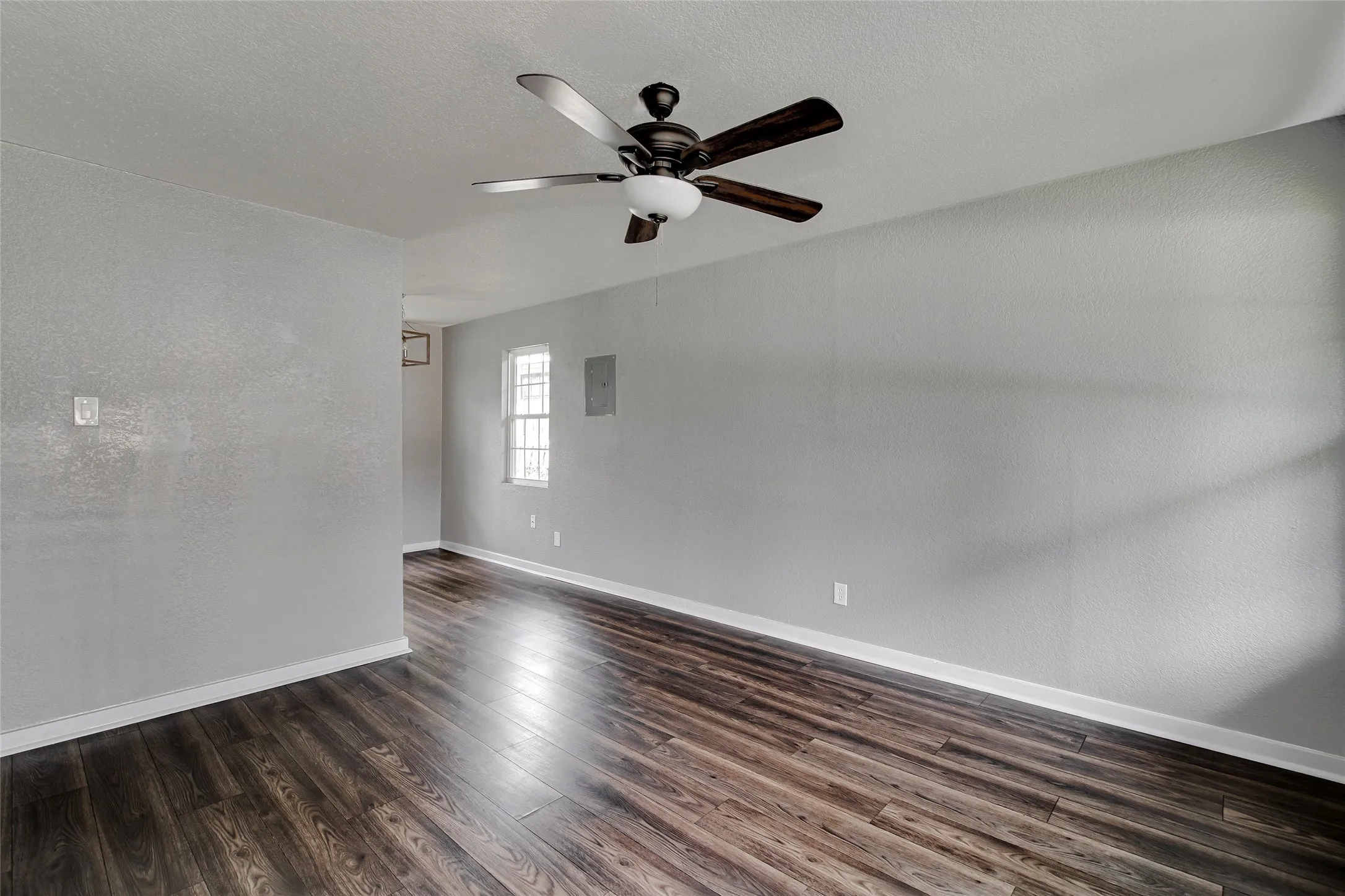 Spacious room featuring wood-finish flooring, light gray walls, white baseboards, and a ceiling fan with integrated lighting