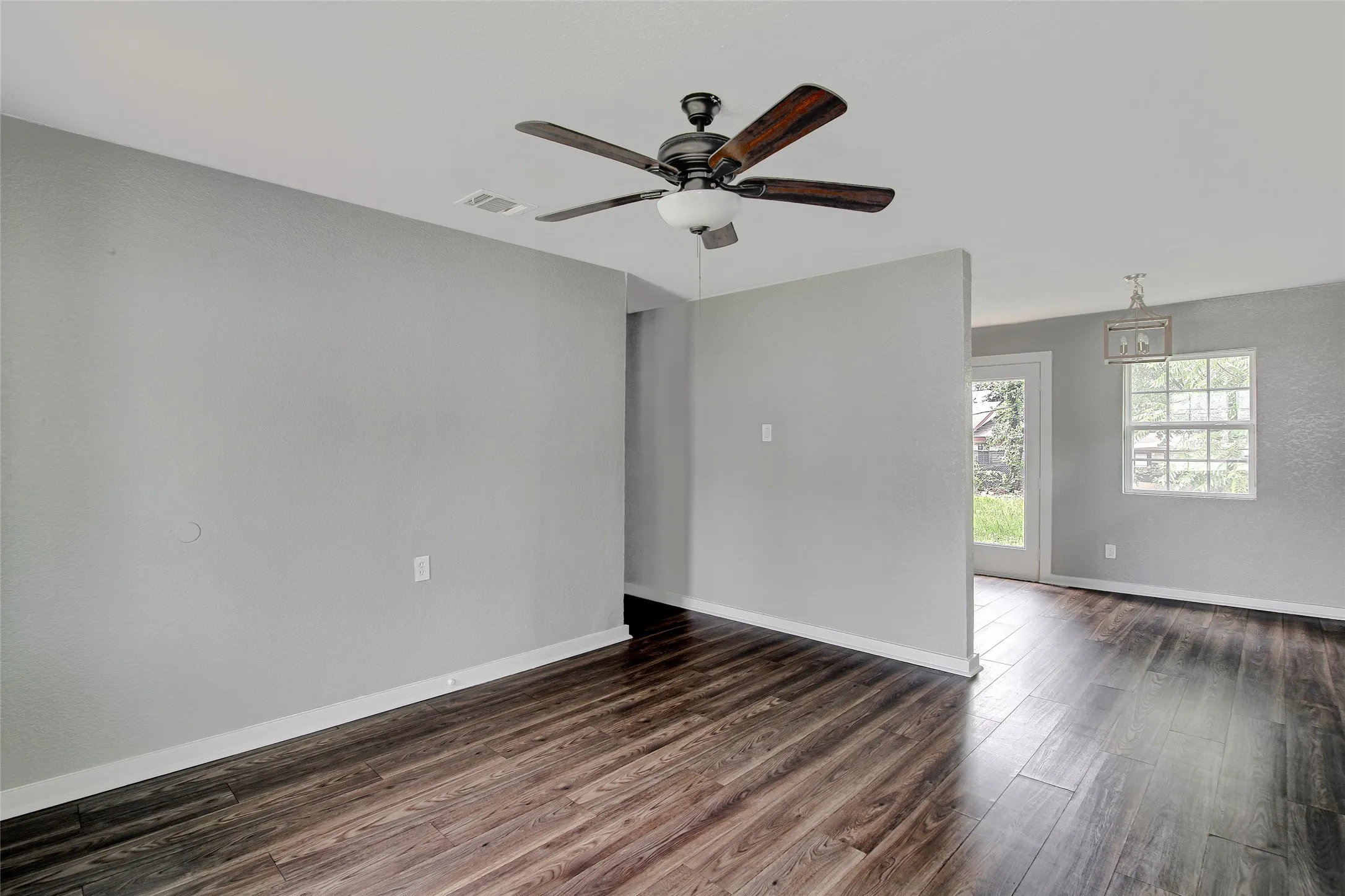 Spacious room with dark wood-finish flooring, light gray walls, and a ceiling fan with integrated lighting