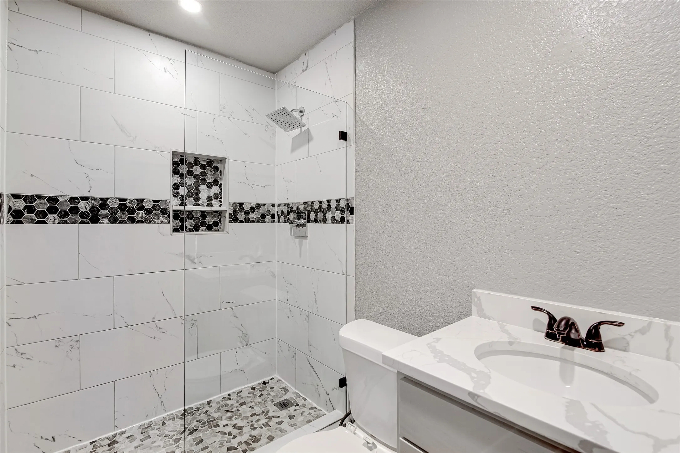 Tiled shower featuring a hex mosaic accent band and two recessed niches