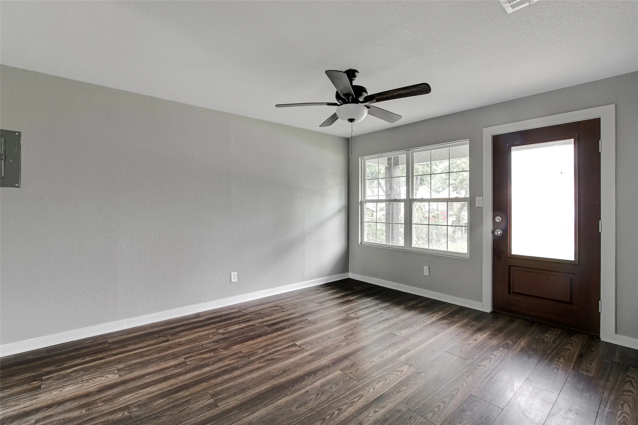 Spacious room featuring wood-finish flooring, light grey walls, white trim, a ceiling fan, and multiple windows