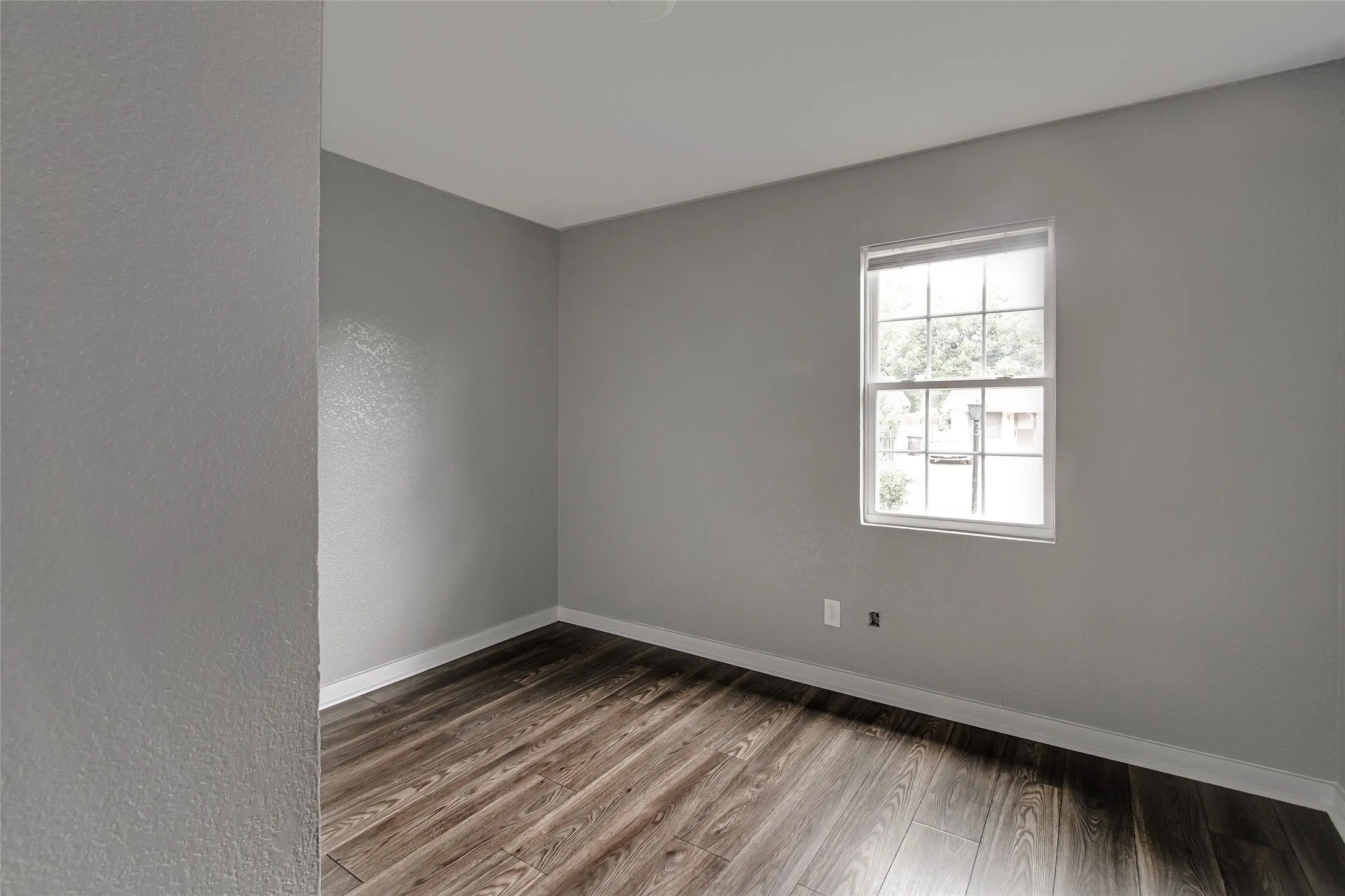 Spacious room featuring wood-finish flooring, light gray walls, and a window with white trim