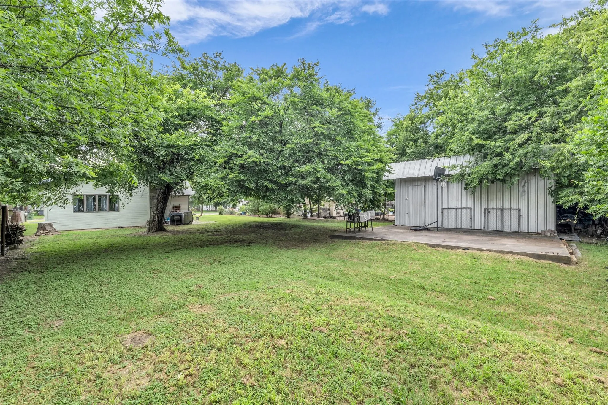 Expansive lawn featuring mature trees and a detached structure with a metal roof