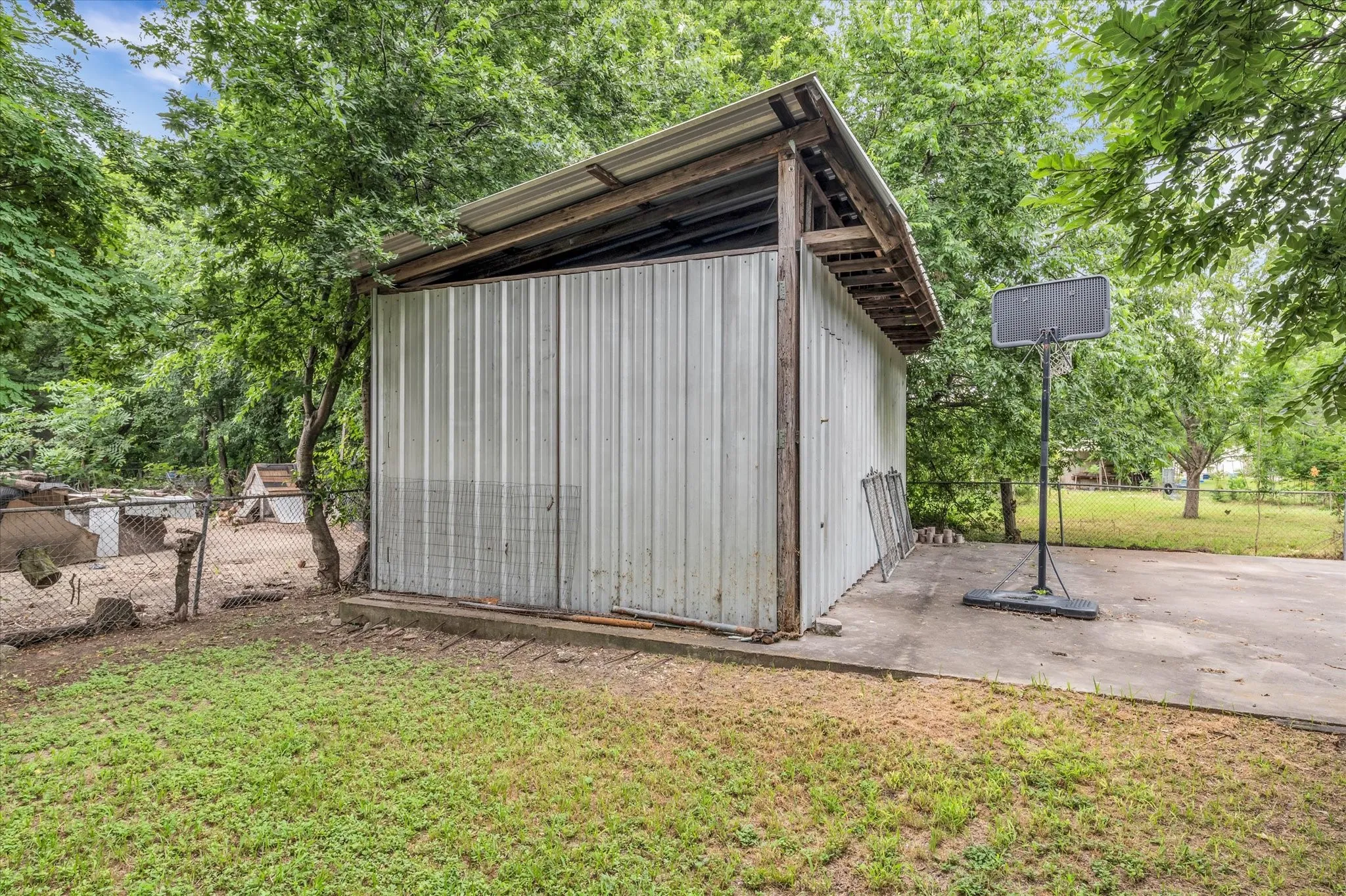 Corrugated metal shed with a lean-to roof structure, featuring a concrete pad and a surrounding grass area