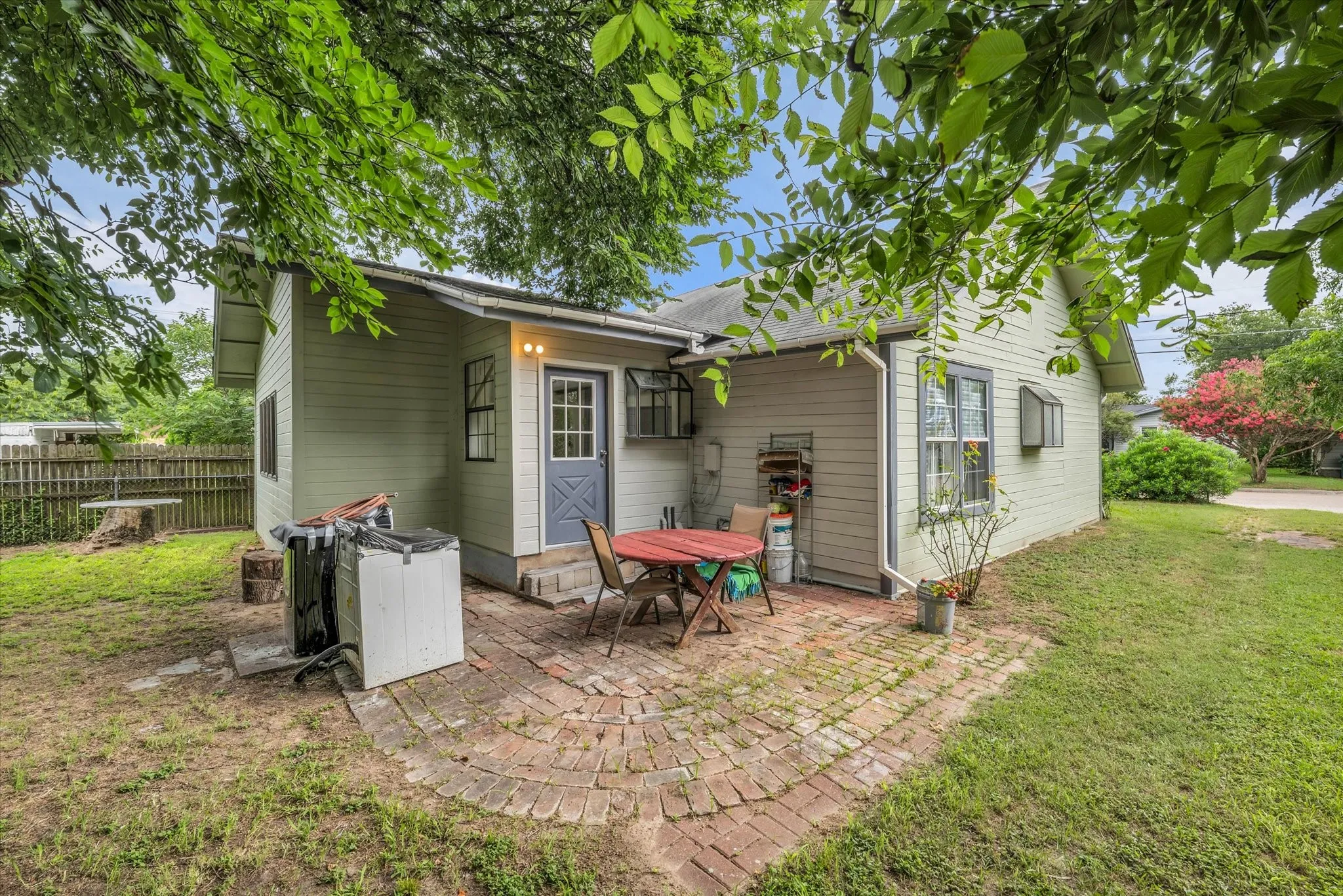 Exterior featuring light green siding, multiple windows, and a brick patio