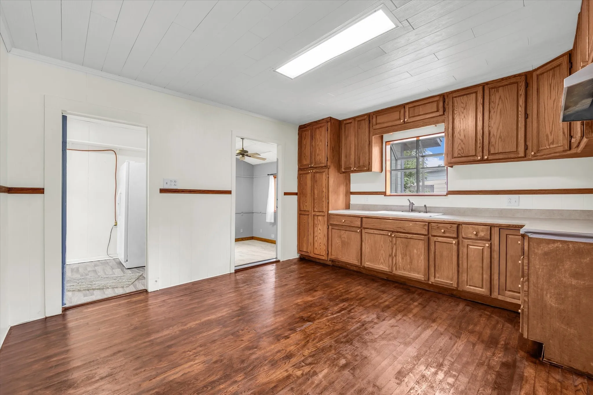 Kitchen featuring extensive wood cabinetry, wood-finish flooring, a white paneled ceiling, and a bay window above the sink