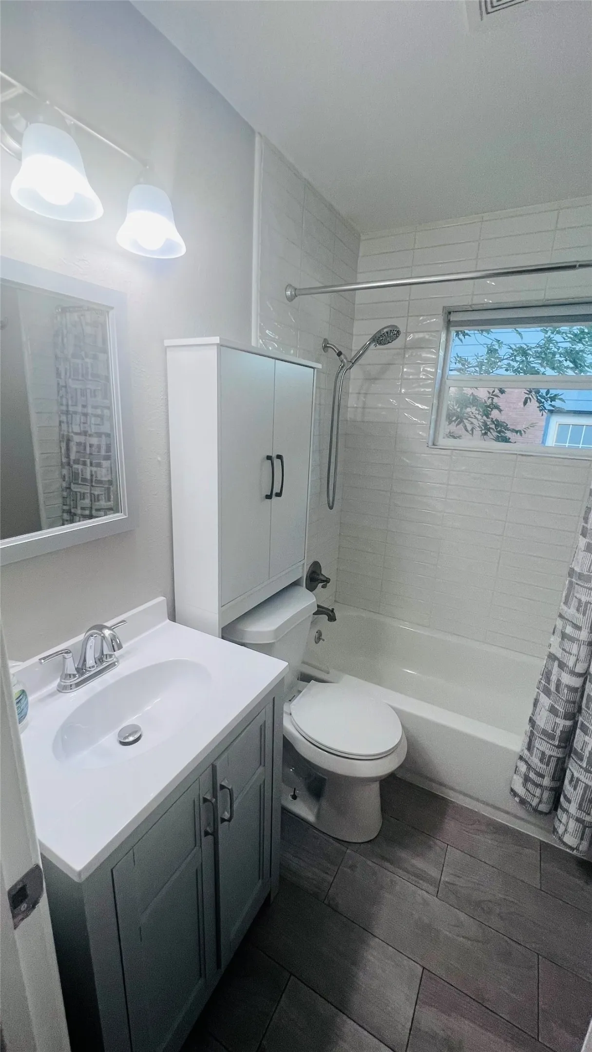 Bathroom featuring a white vanity with integrated sink, wood-finish flooring, a full bathtub with shower, and a built-in storage cabinet