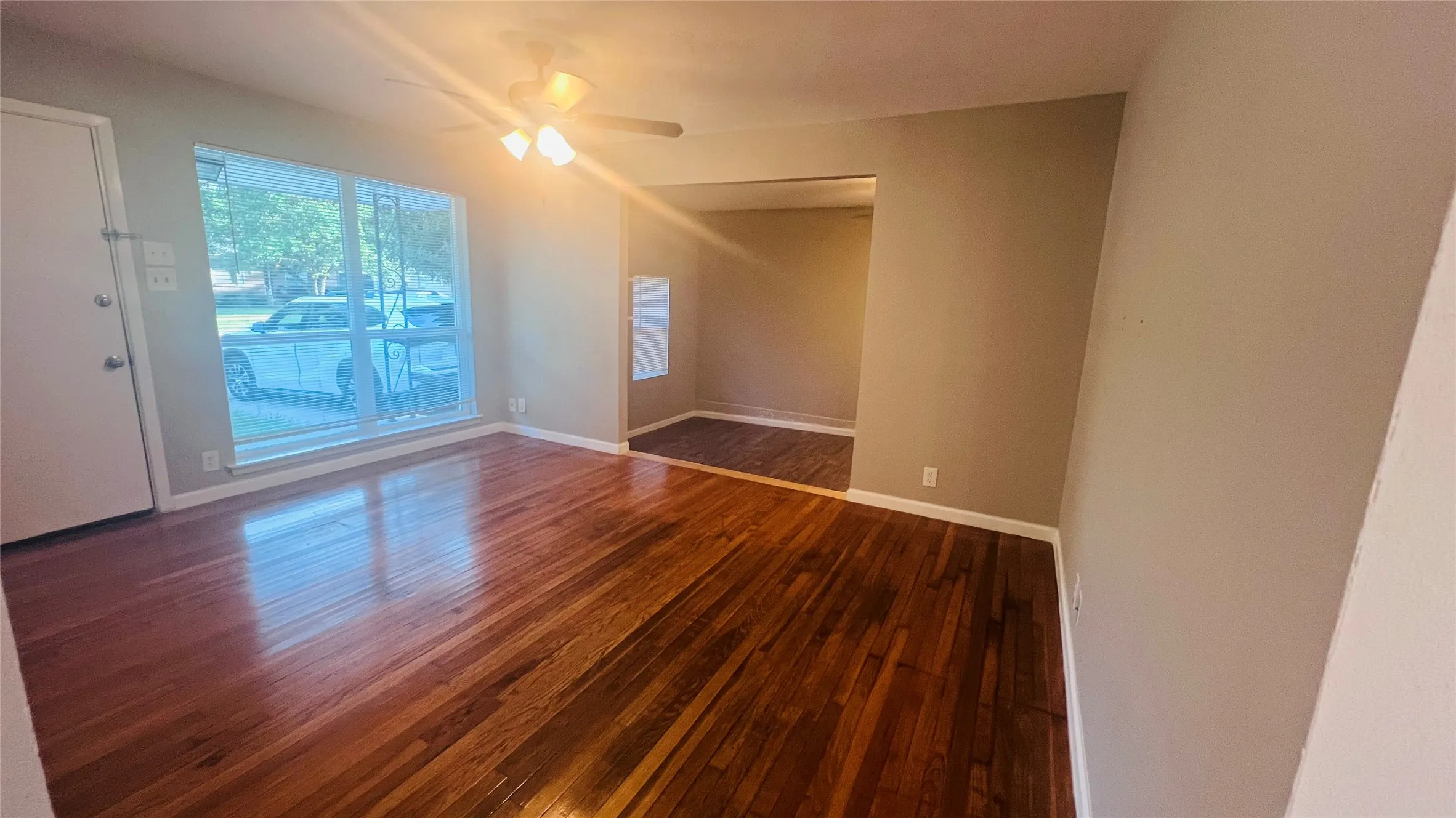 Spacious room featuring wood-finish flooring, a large window, a ceiling fan with integrated lighting, and neutral wall tones