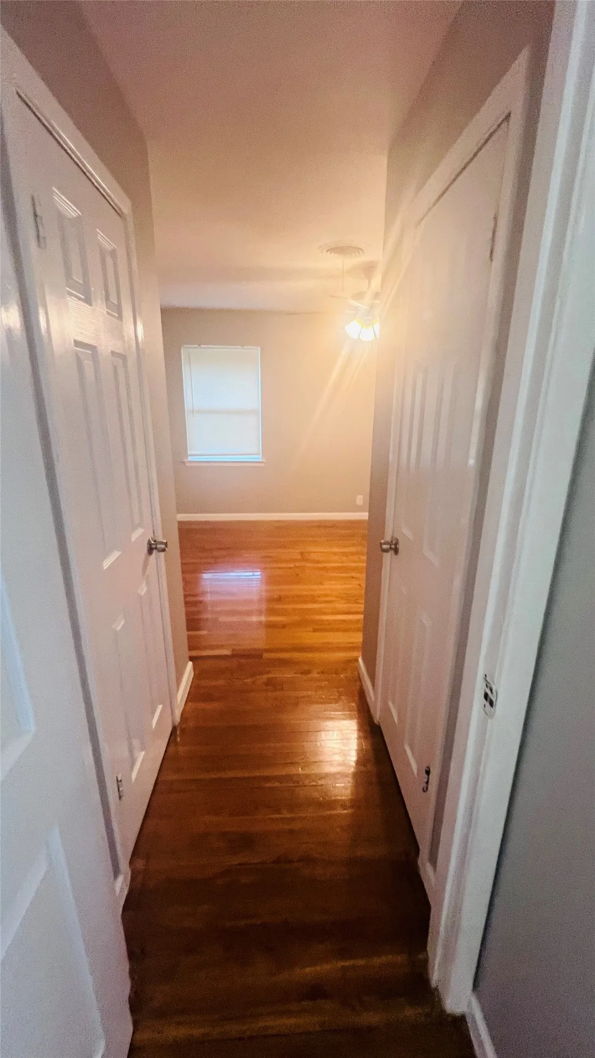 Hardwood flooring runs through the hallway into a room with a window and ceiling light fixture