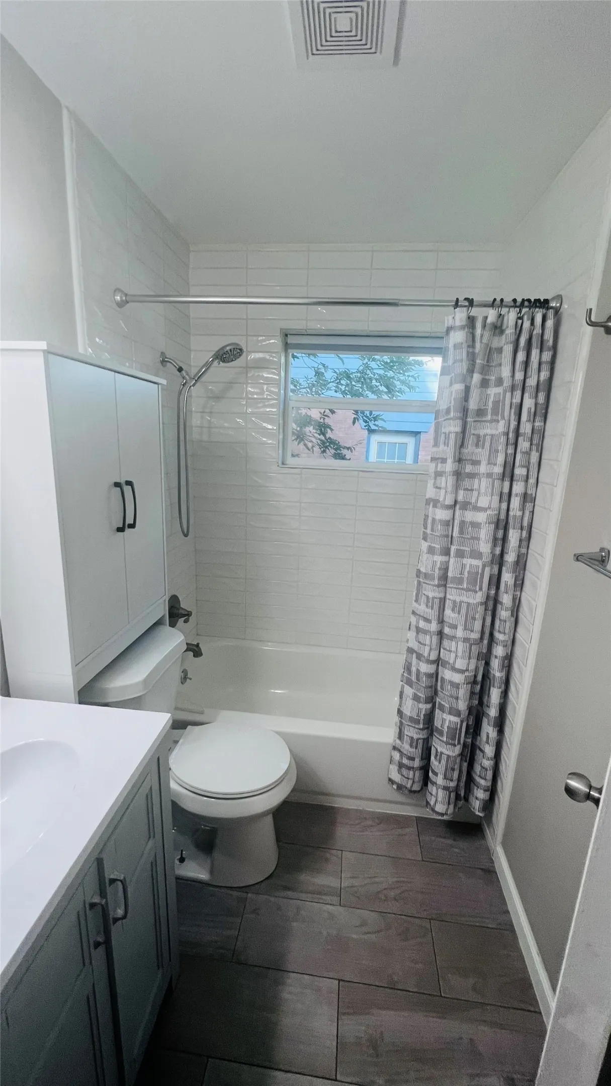 Bathroom featuring a white subway tile surround, a single window, wood-finish flooring, a white vanity with a white countertop, and a built-in storage cabinet