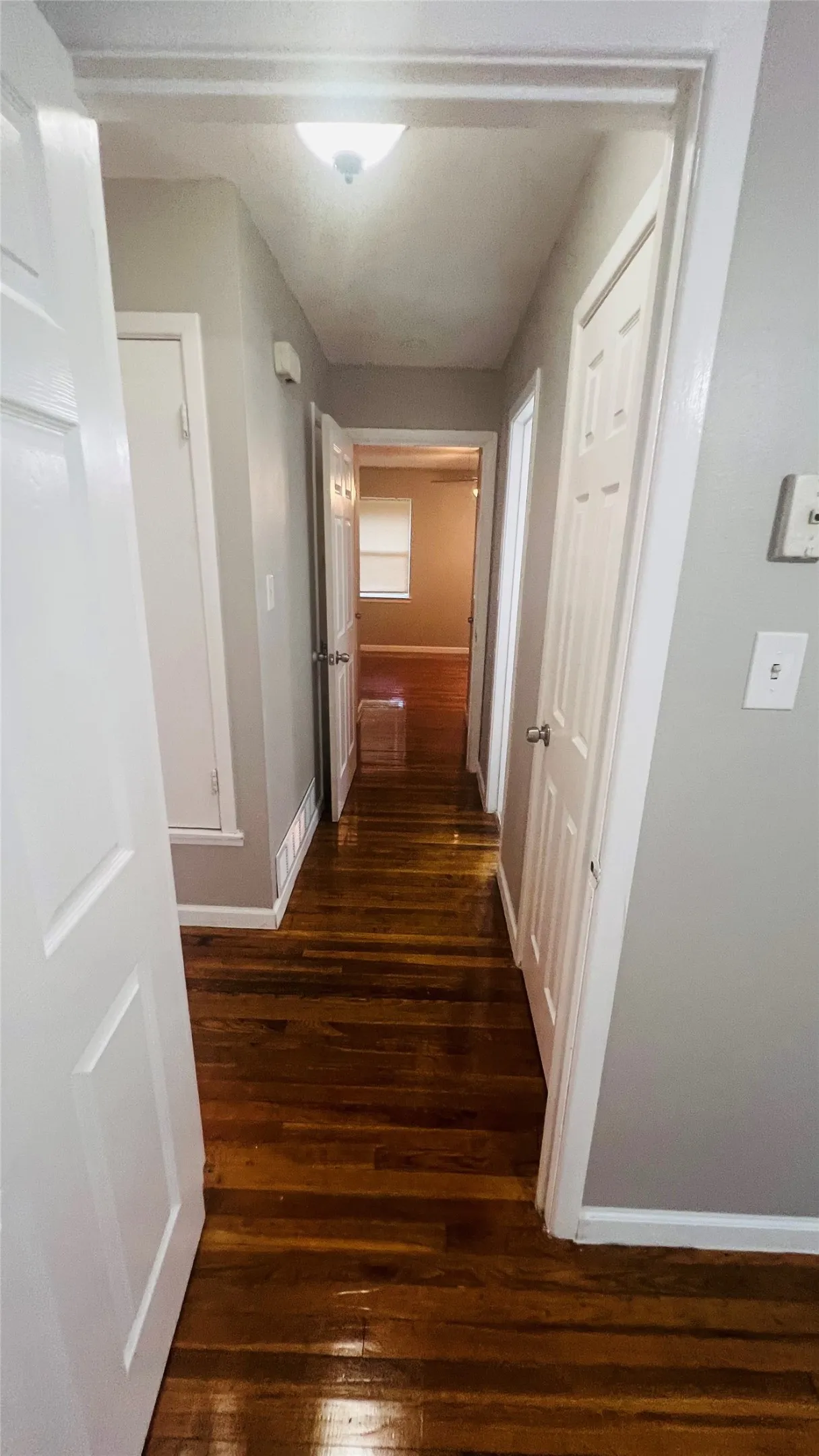 Hallway featuring rich wood-finish flooring, light gray wall paint, white trim, and a ceiling-mounted light fixture
