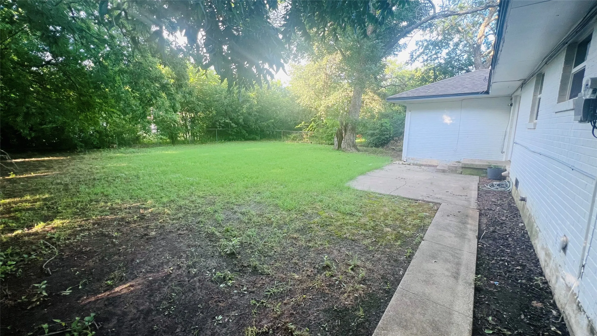 Expansive rear yard featuring a large grass area, mature trees, concrete patio, and a concrete pathway along the residence