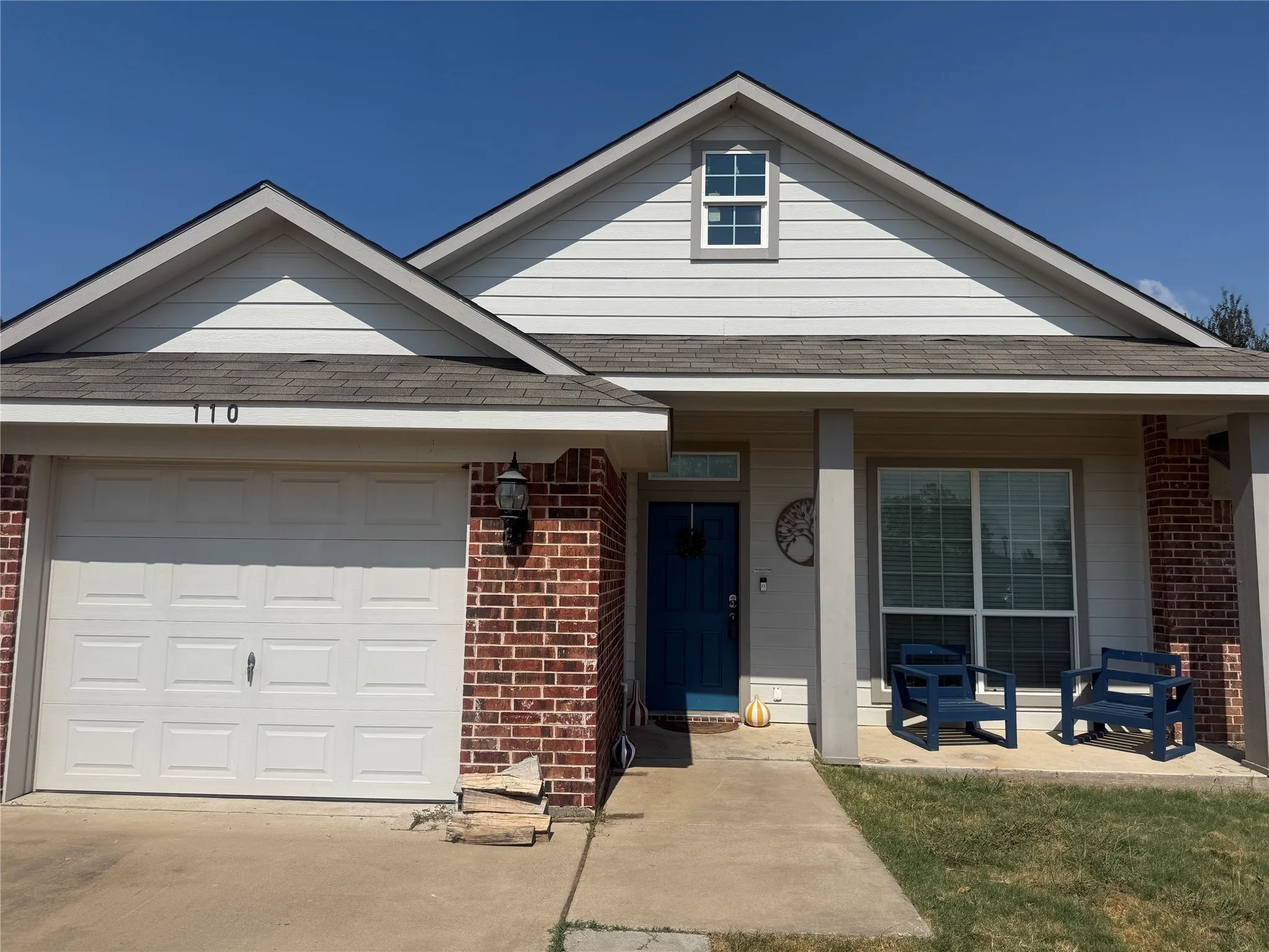 Exterior featuring a partial brick facade, horizontal siding, a covered front porch, and an attached garage with a panel door