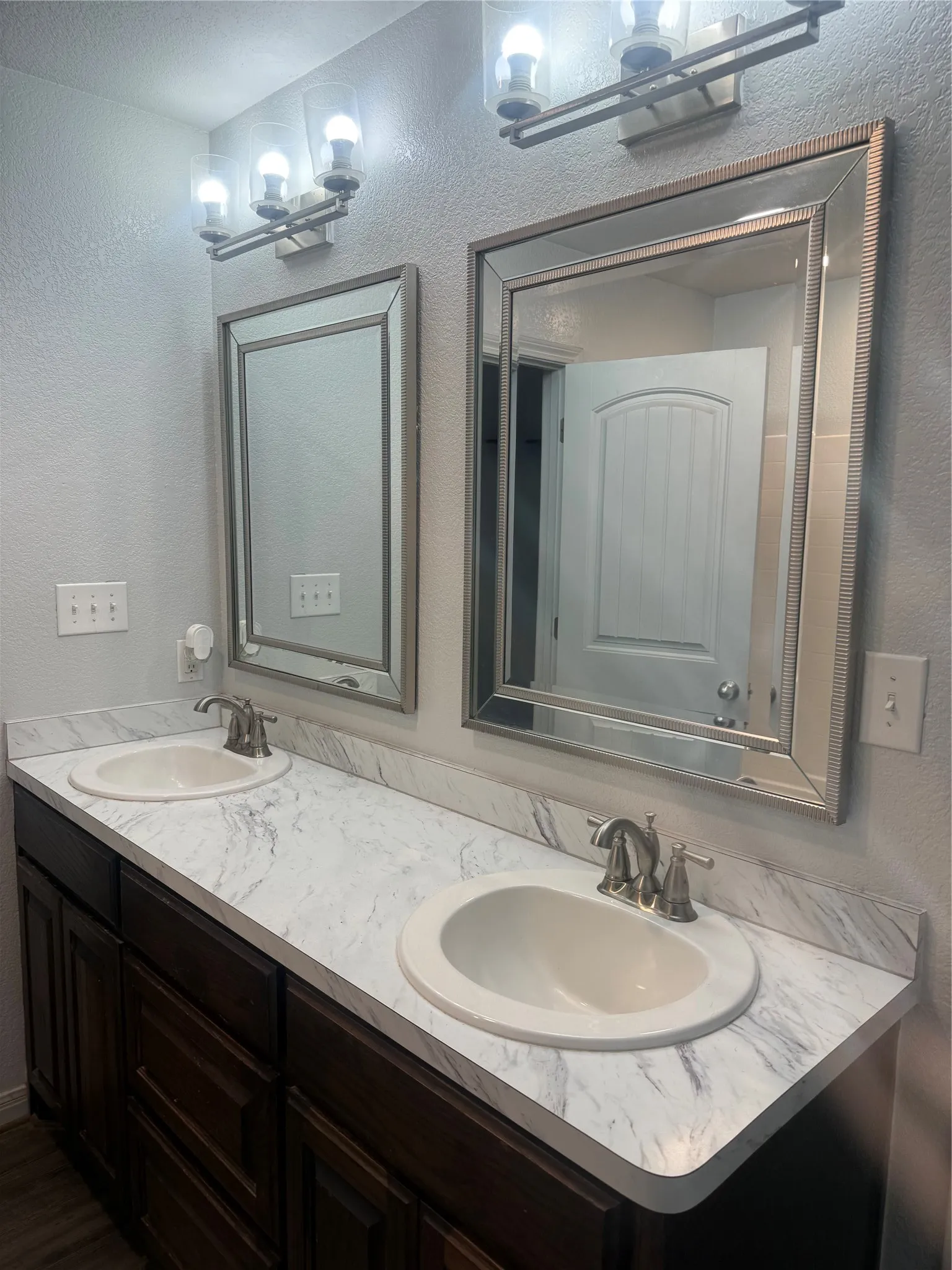 Dual vanity with integrated sinks, white countertops, dark wood-finish cabinetry, and two framed mirrors