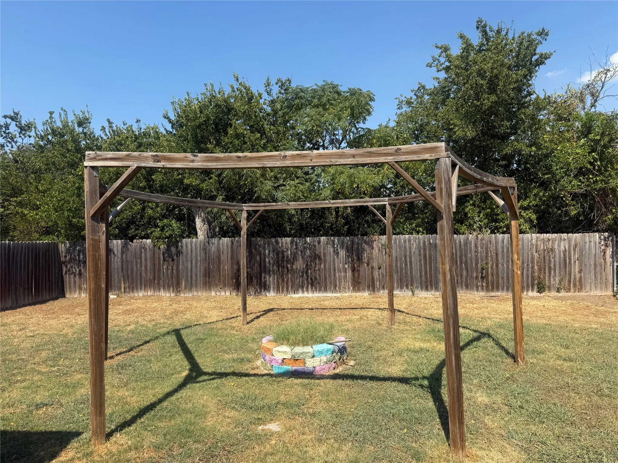 Outdoor pergola structure with a wood privacy fence and mature trees