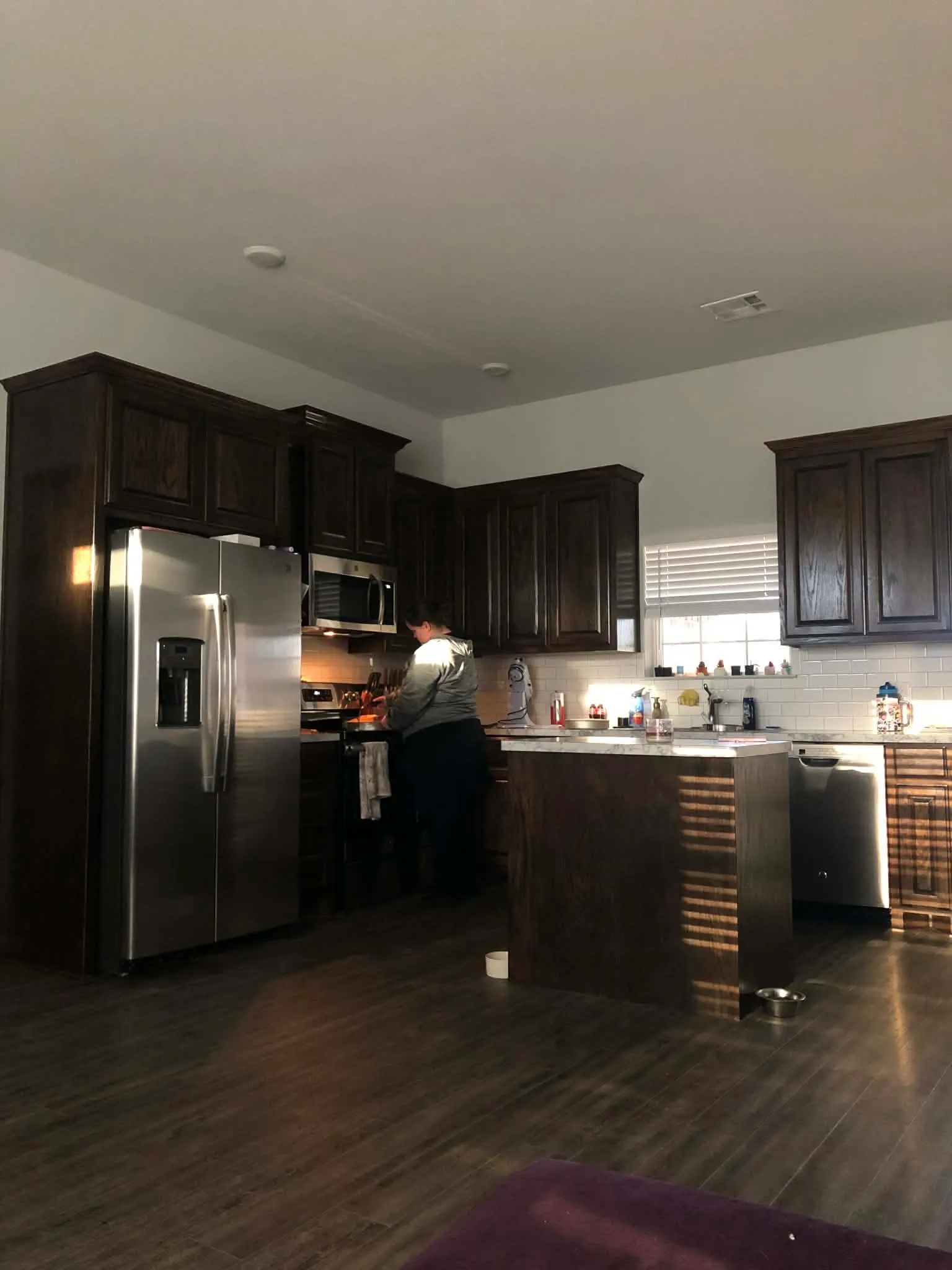 Kitchen featuring dark wood cabinetry, stainless steel appliances, a white subway tile backsplash, and an island with a light-colored countertop