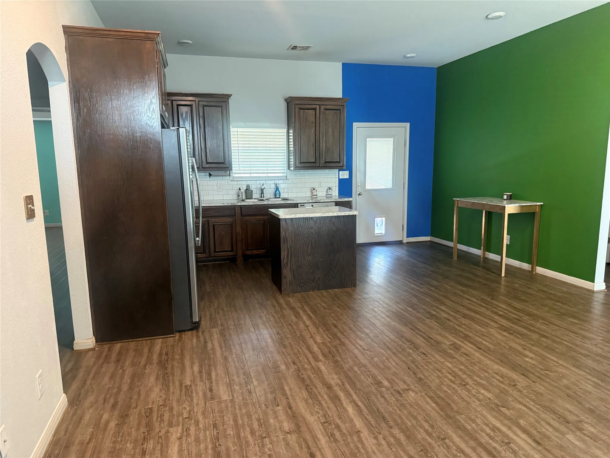 Wood-finish flooring throughout, dark wood-finish cabinetry, kitchen island with countertop, and subway tile backsplash