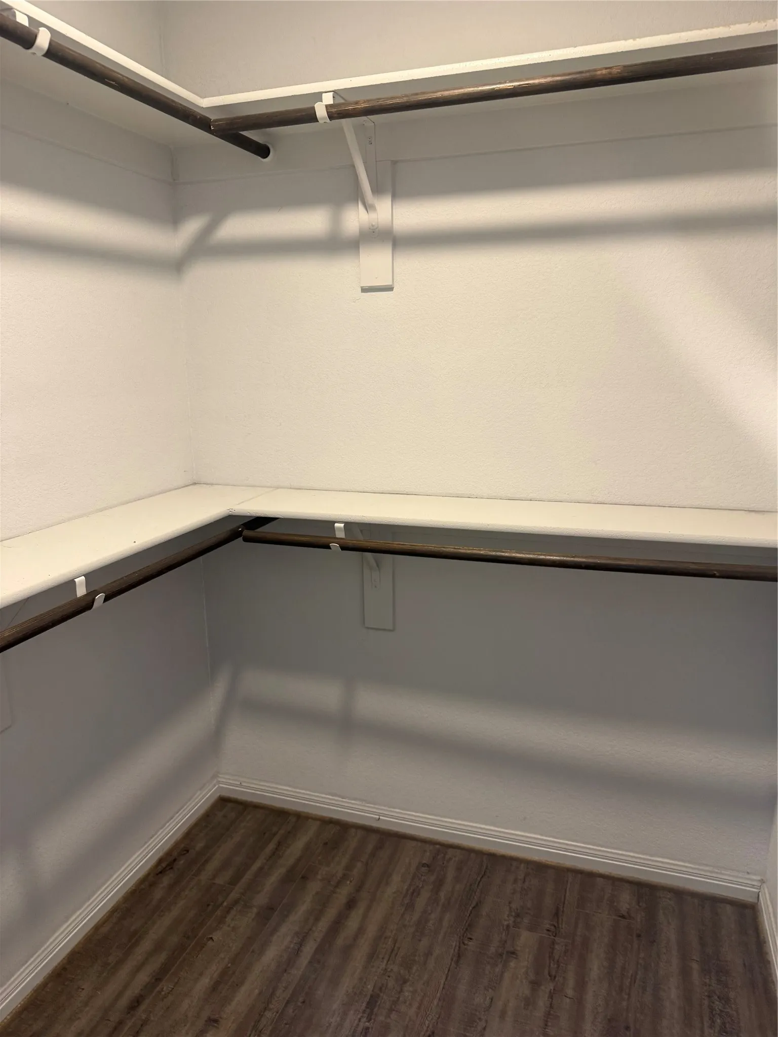 Walk-in closet featuring wood-finish flooring, white painted walls, and built-in shelving with hanging rods