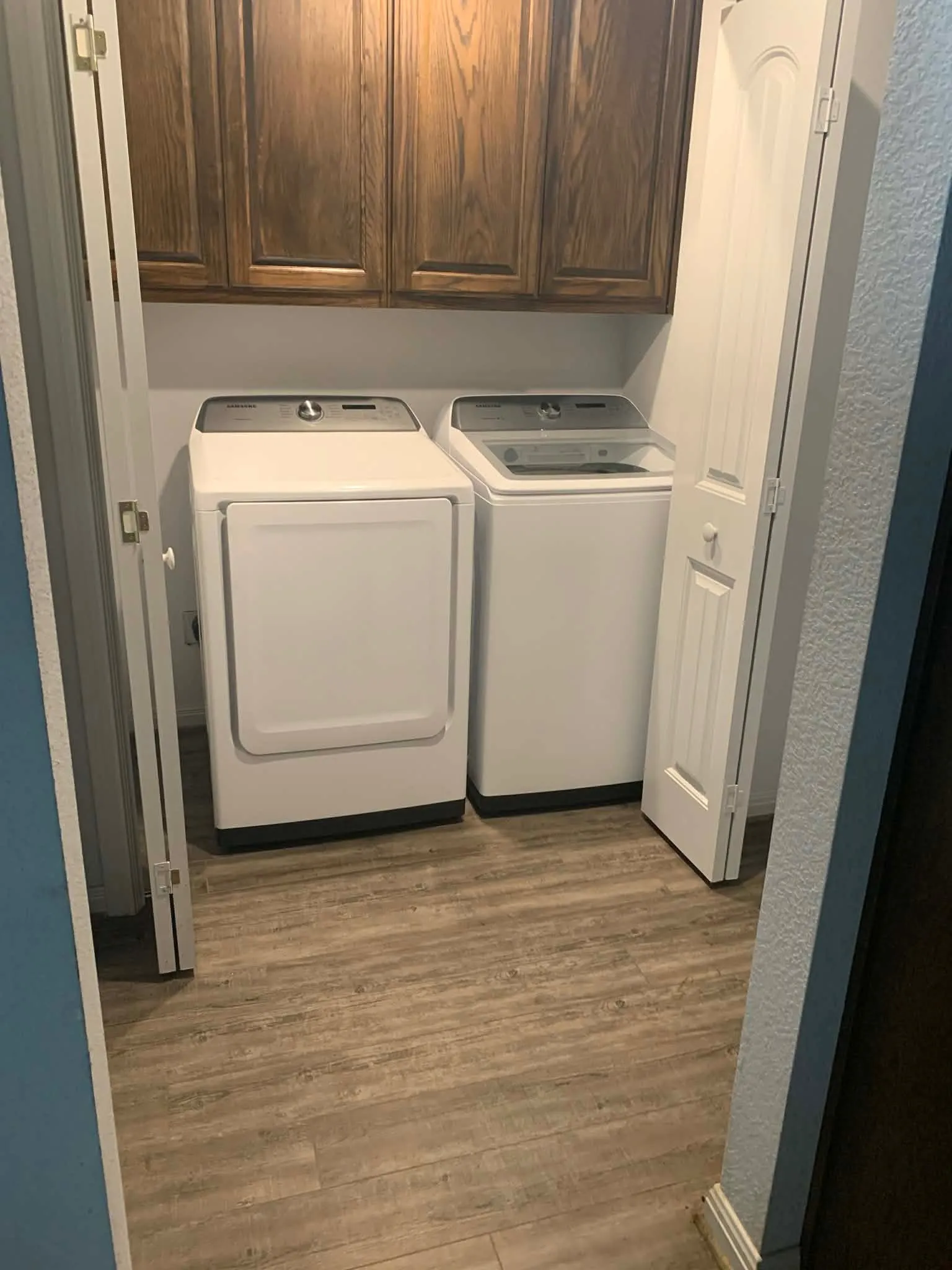 Dedicated laundry area featuring wood-finish flooring, overhead wood cabinetry, and bi-fold closet doors