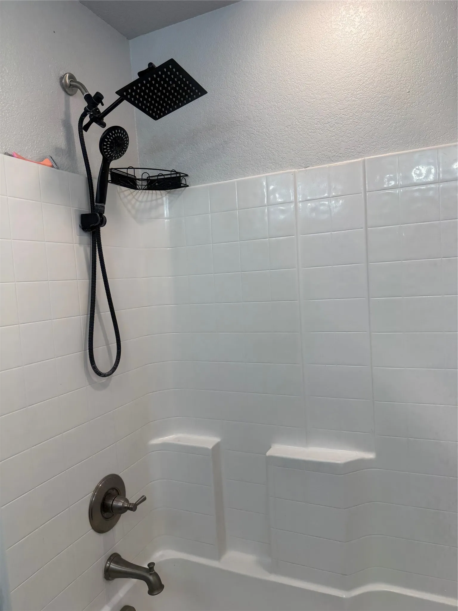 Bathtub with white subway tile surround, matte black rainfall shower head, and bronze fixtures