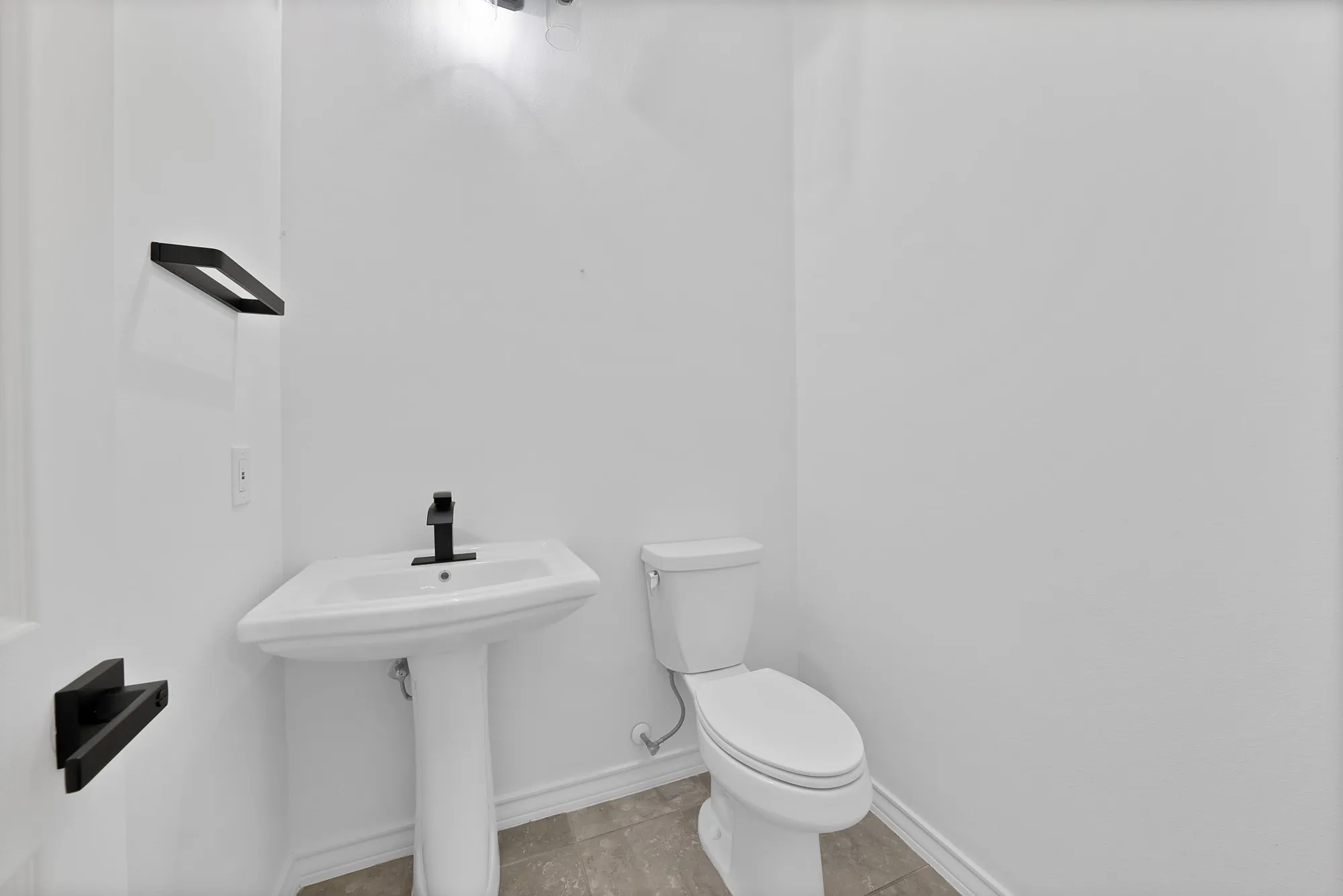 Pedestal sink with a matte black faucet, complemented by a contemporary towel bar and toilet paper holder