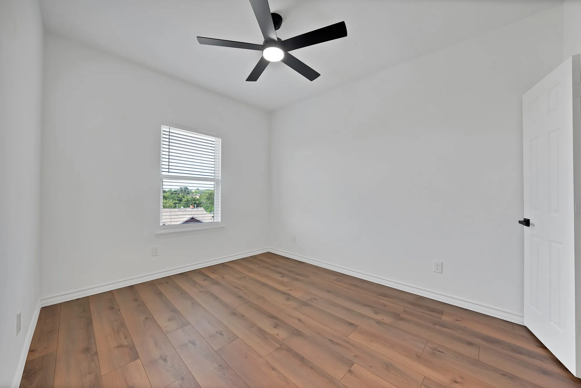 Spacious room with wood-finish flooring, white baseboards, and a modern ceiling fan with integrated lighting