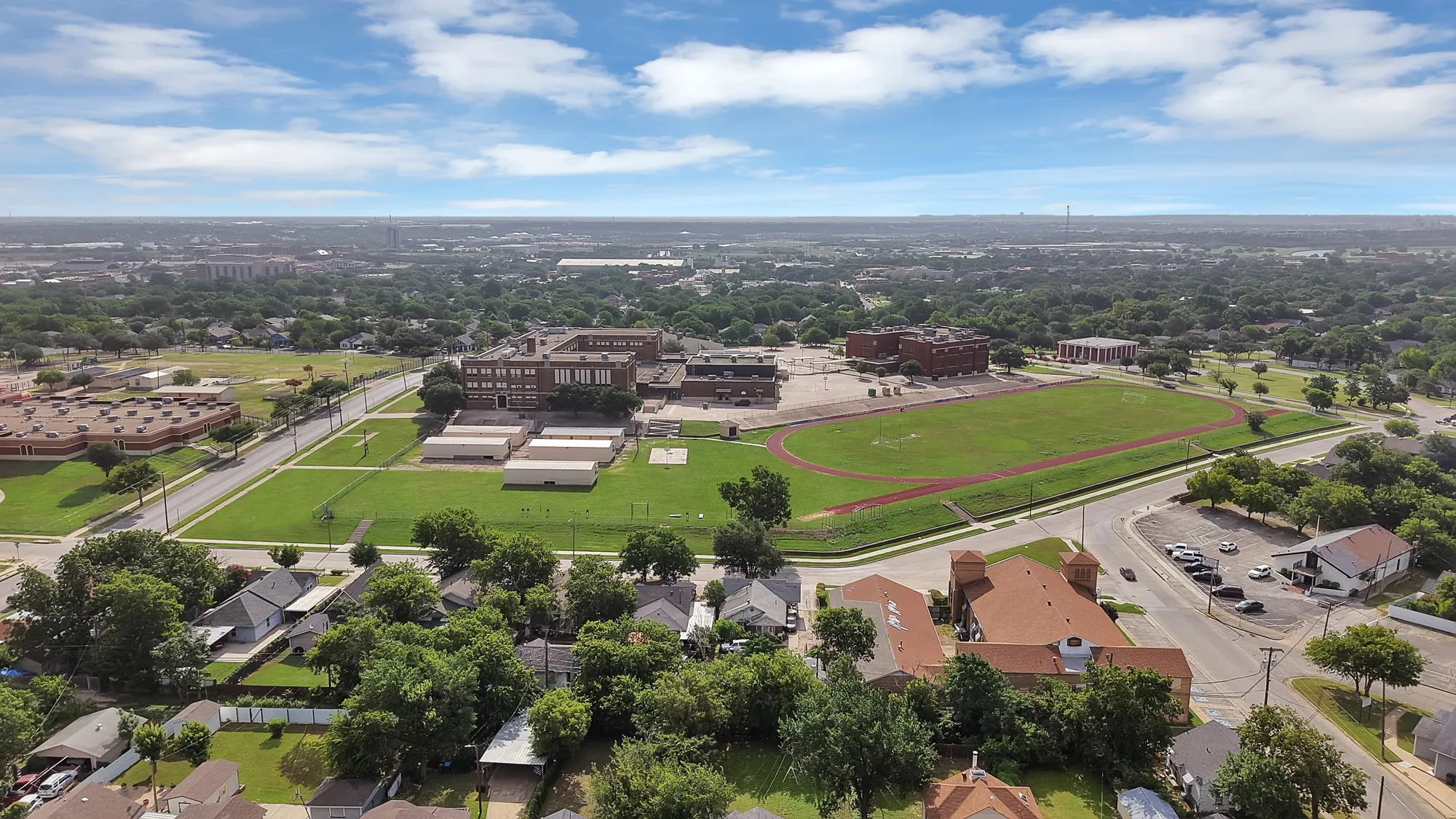 Expansive institutional campus featuring a large athletic field with a running track, multiple brick buildings, and paved parking areas
