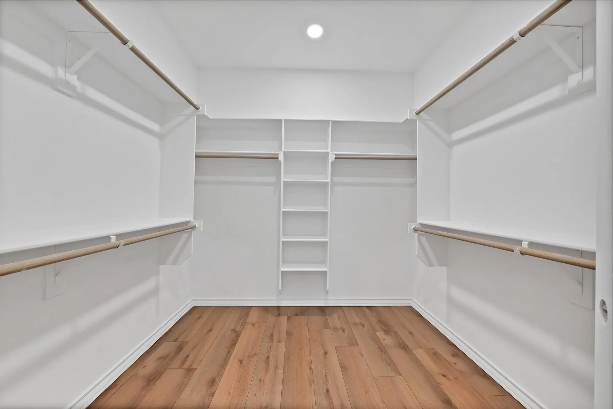 Spacious walk-in closet featuring wood-finish flooring, recessed lighting, white built-in shelving, and multiple hanging rods