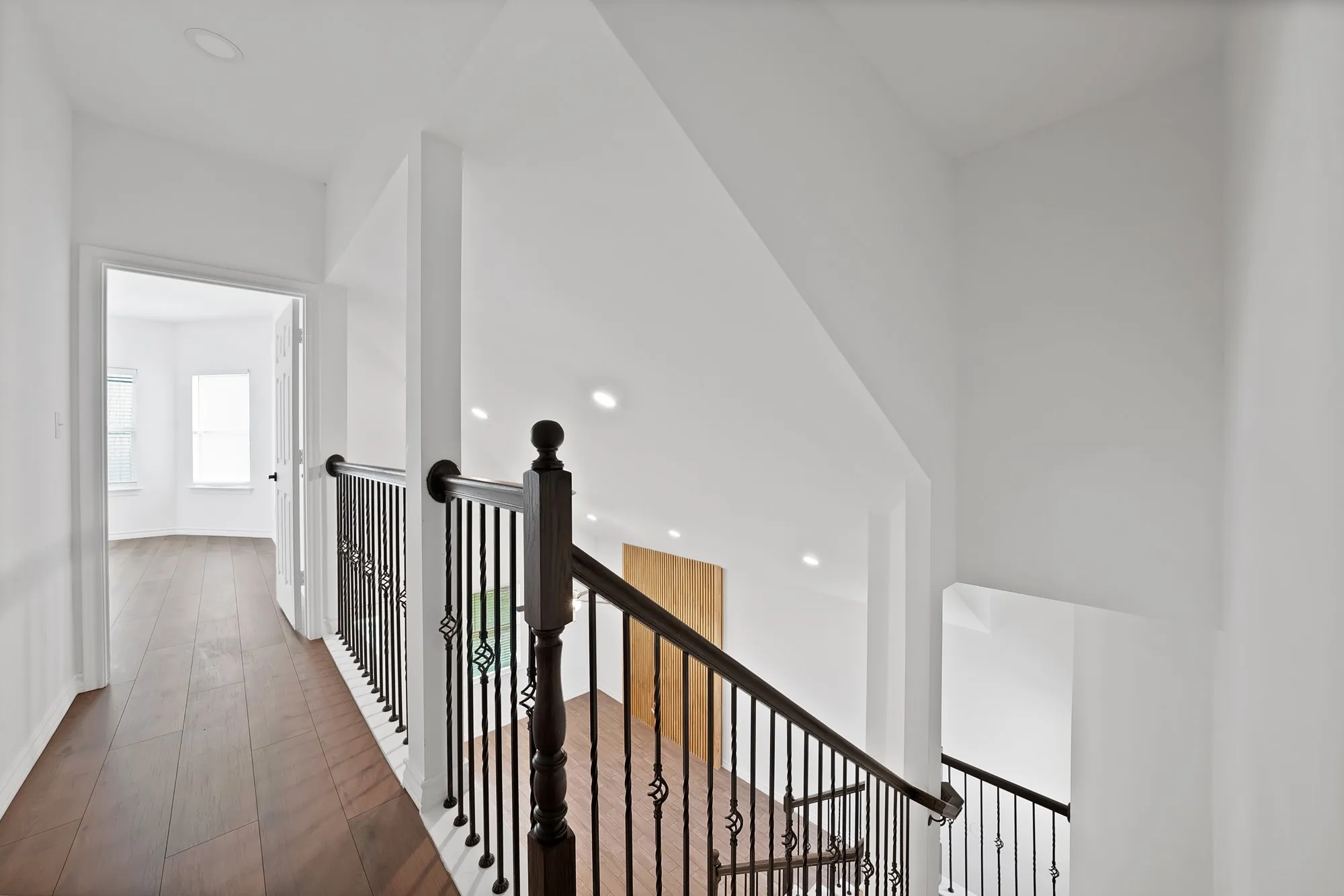 Hallway featuring wood-finish flooring, recessed lighting, and a dark wood newel post with wrought iron balusters