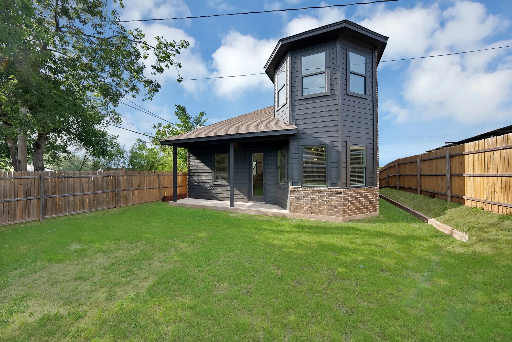 Backyard featuring a wood privacy fence, a covered patio, and a two-story structure with dark siding and a brick base