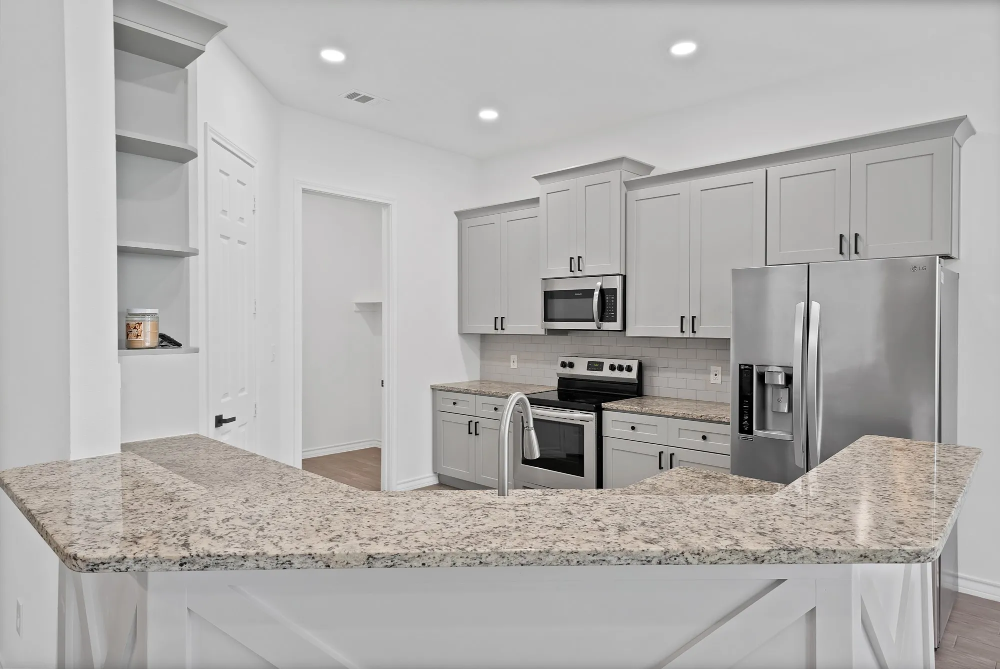 Modern kitchen featuring light-toned cabinetry, stainless steel appliances, speckled stone countertops, and a subway tile backsplash