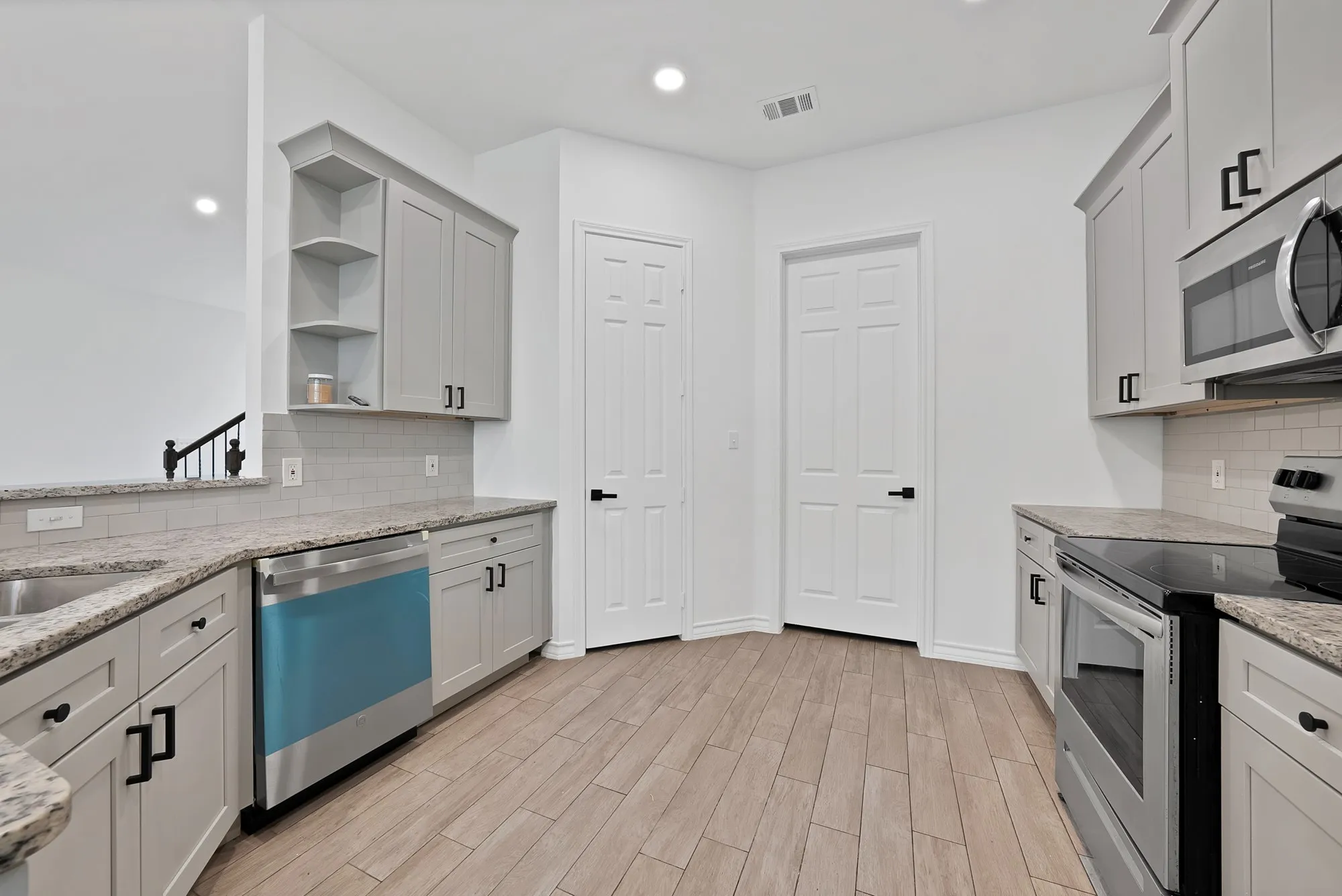 Kitchen featuring light wood-finish flooring, light gray cabinetry with black hardware, granite-style countertops, stainless steel appliances, and a tile backsplash