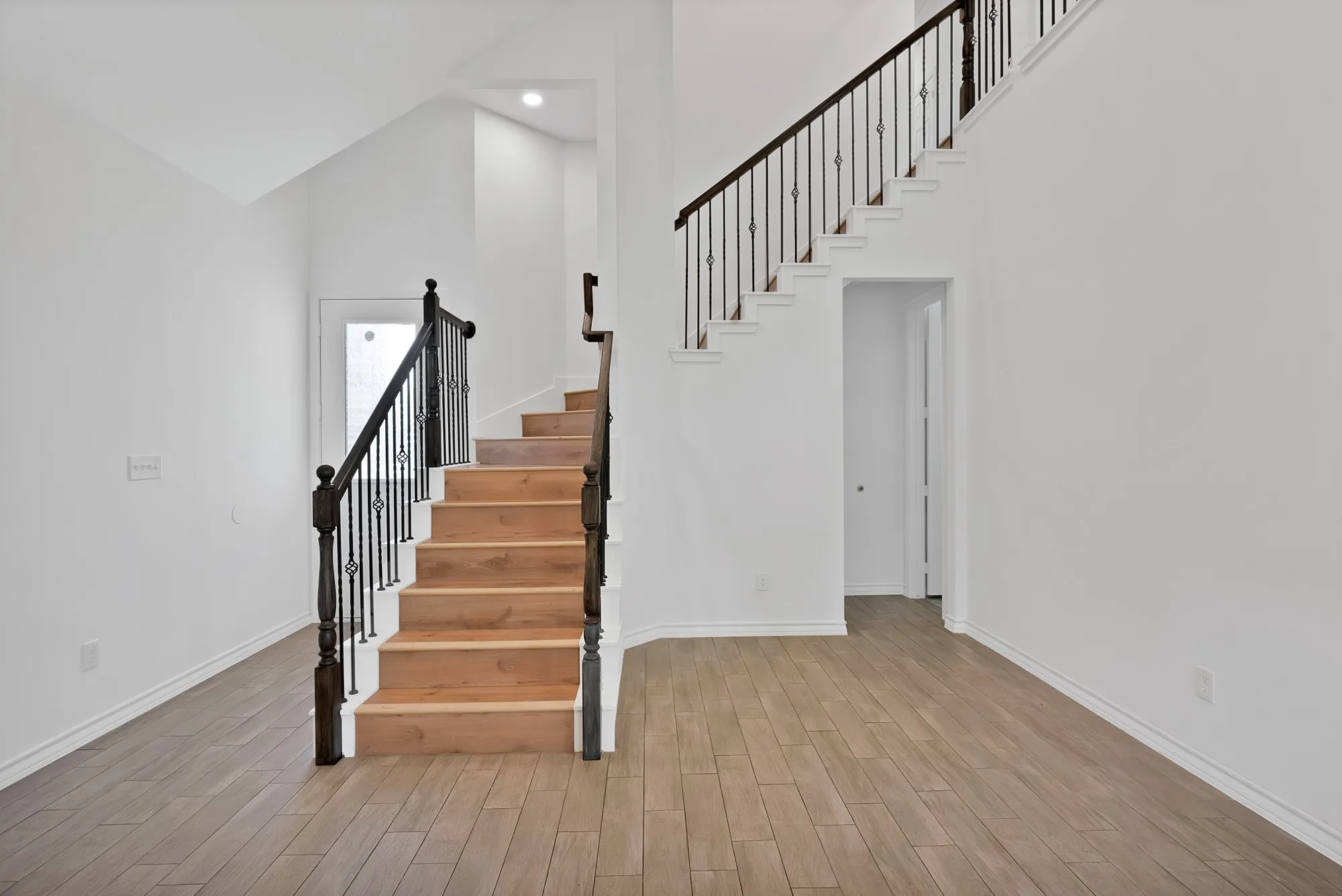 Grand staircase featuring wood-finish treads and risers with decorative wrought iron balusters and dark wood newel posts