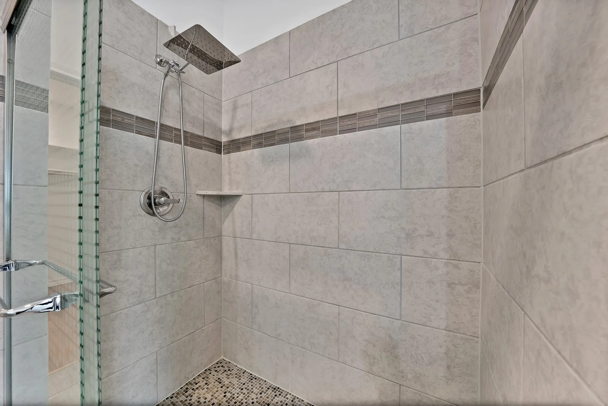 Shower with tiled walls, pebble flooring, integrated shower niche, and a rain shower head with an additional handheld shower fixture
