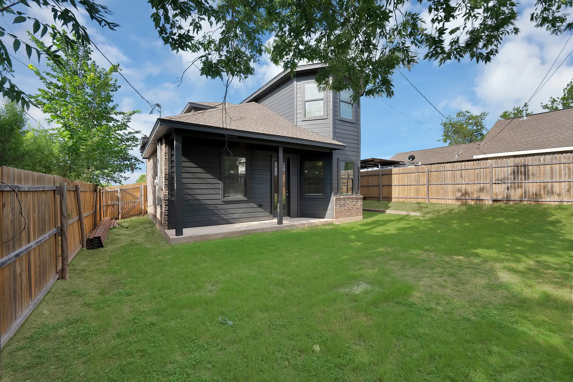Expansive backyard featuring a large grassy area, privacy fencing, and a covered patio area