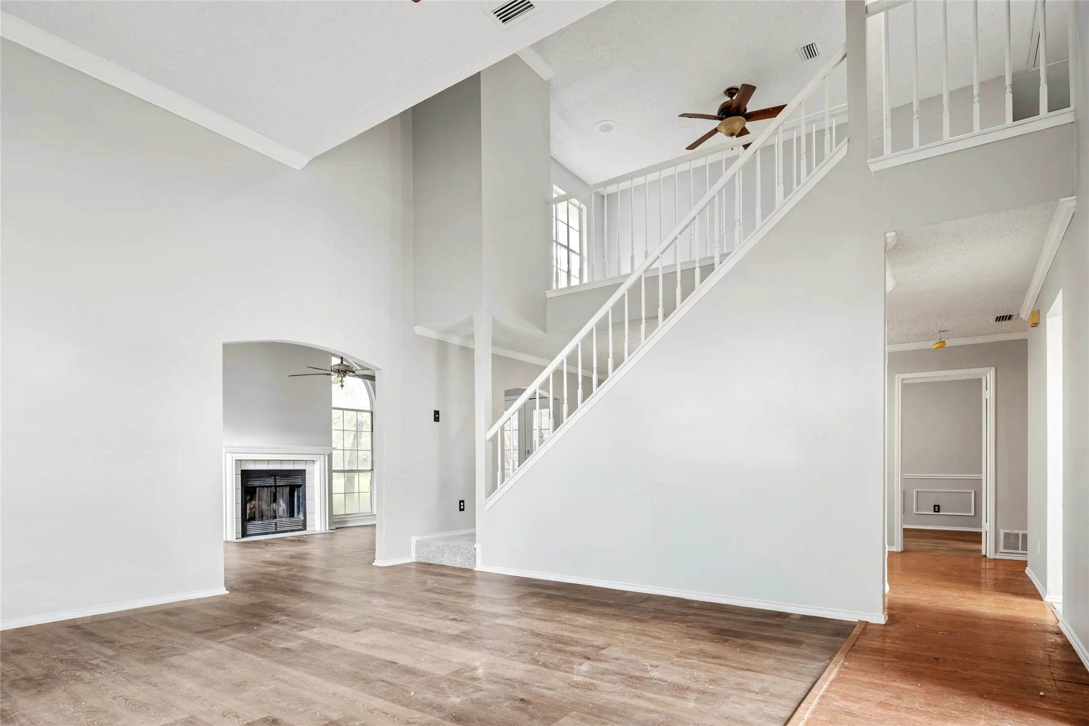 Two-story foyer featuring wood-finish flooring, a white spindle staircase, and a ceiling fan