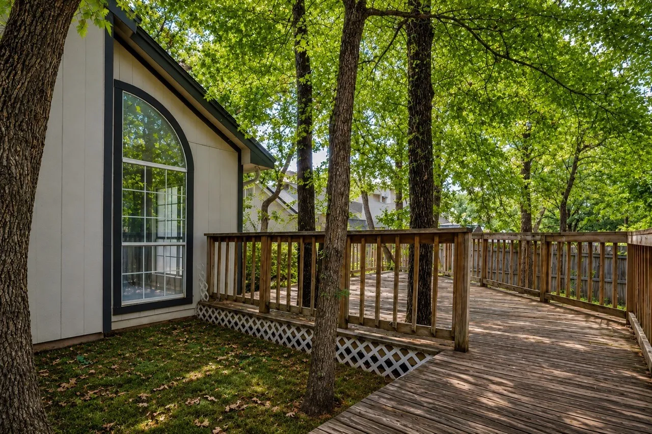 Arched window with grilles and dark trim, alongside a wood deck with railings