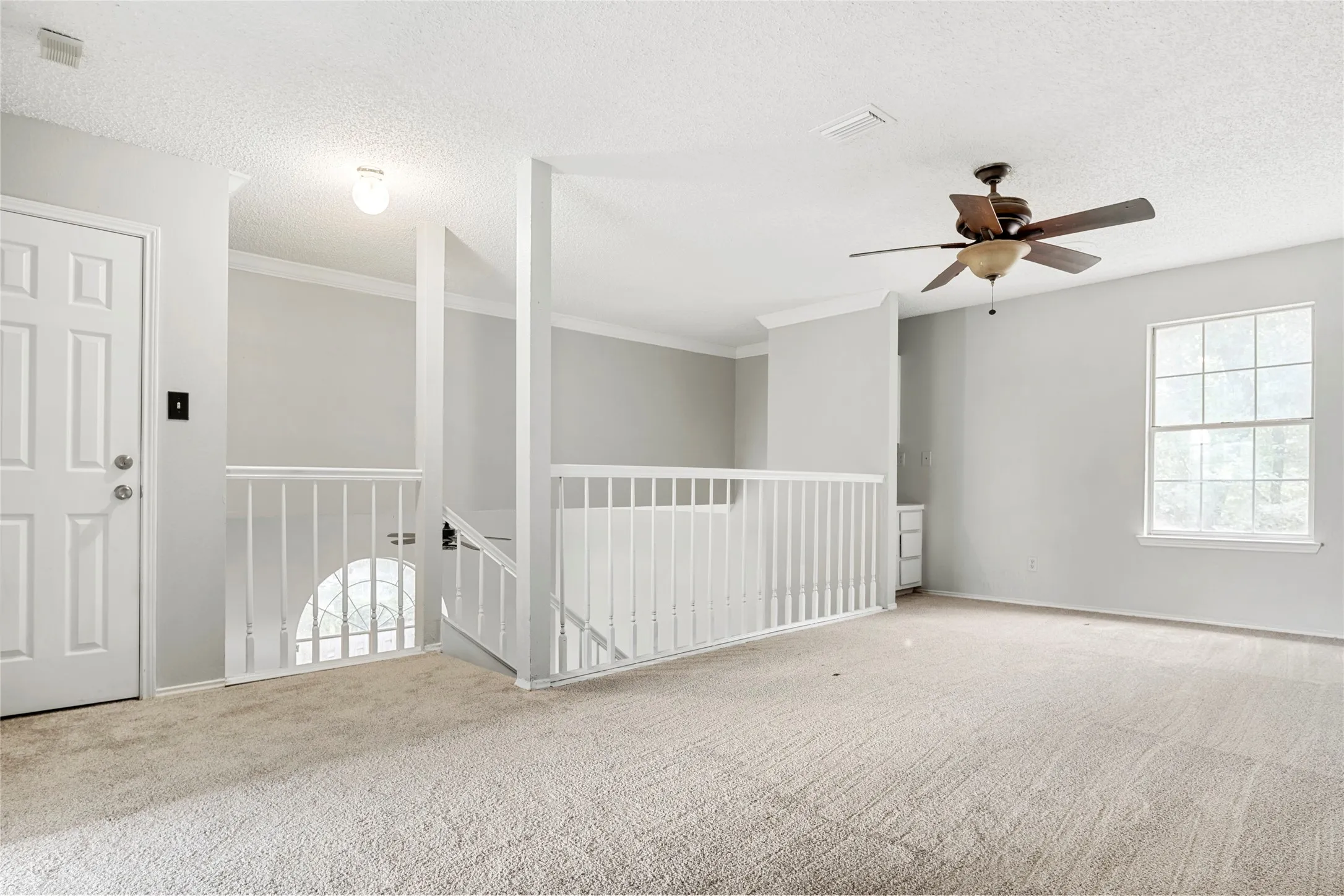 Carpeted upper-level landing featuring white railings and trim, a six-panel door, and a ceiling fan with light fixture