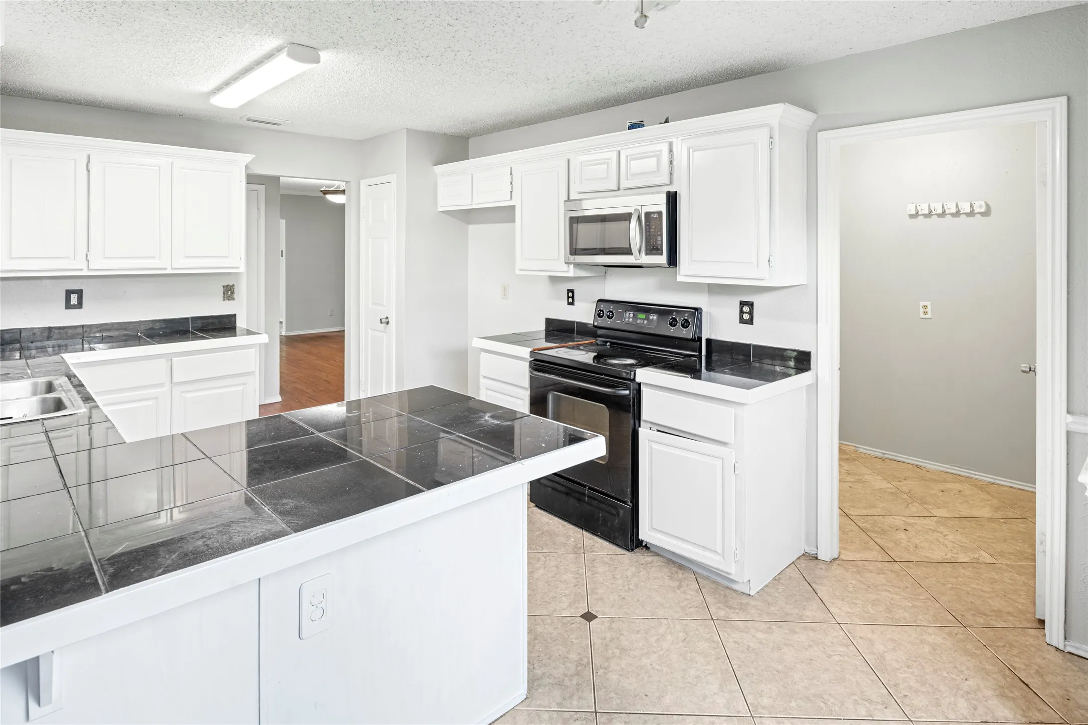 White cabinetry kitchen featuring a built-in microwave, black electric range, and dark tile countertops with a matching backsplash
