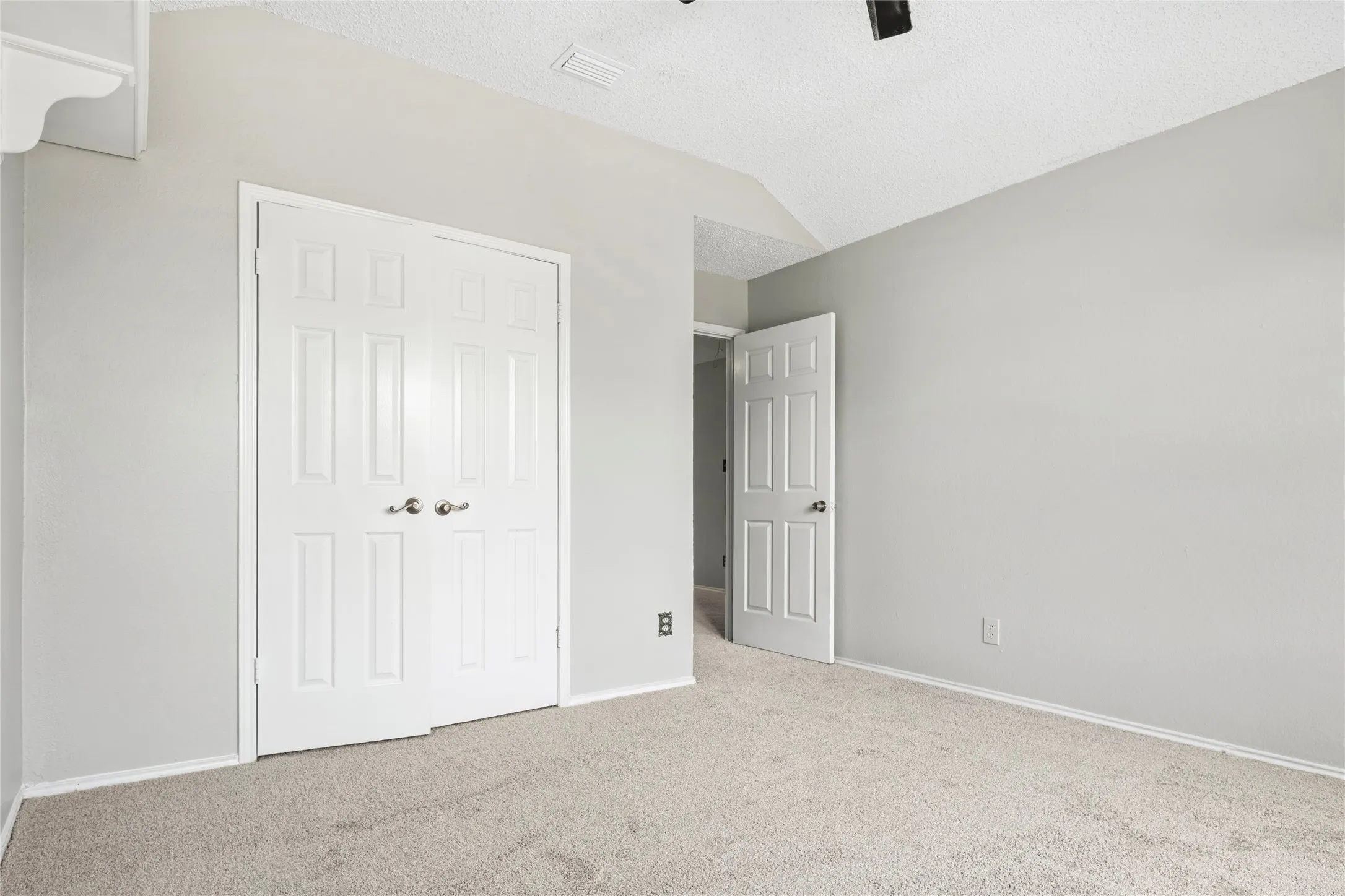 Carpeted room featuring a double-door closet with paneled doors, vaulted ceiling, and light gray wall paint