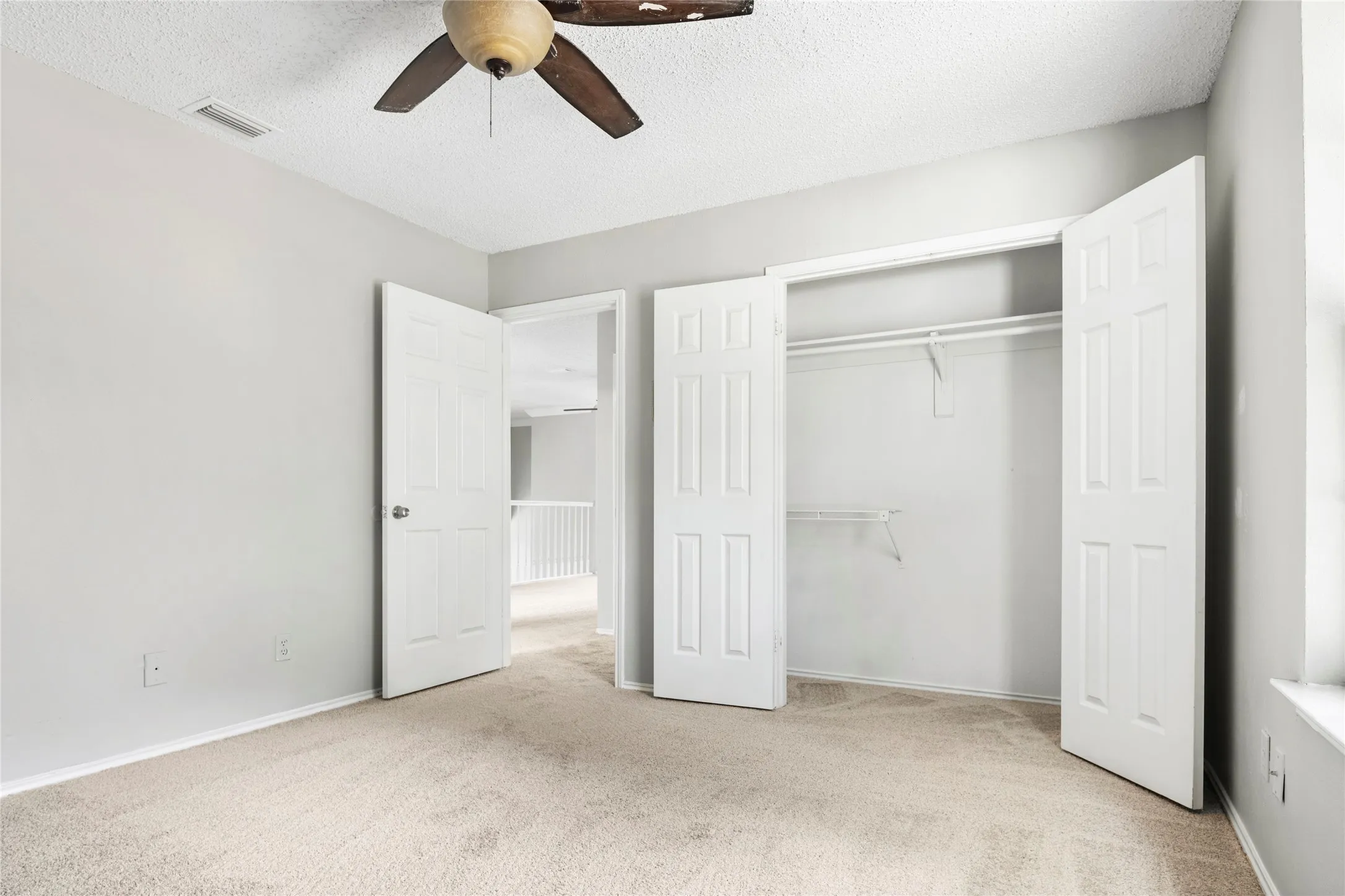 Carpeted room featuring a ceiling fan with wood-finish blades, a closet with bi-fold doors, and a window providing natural light