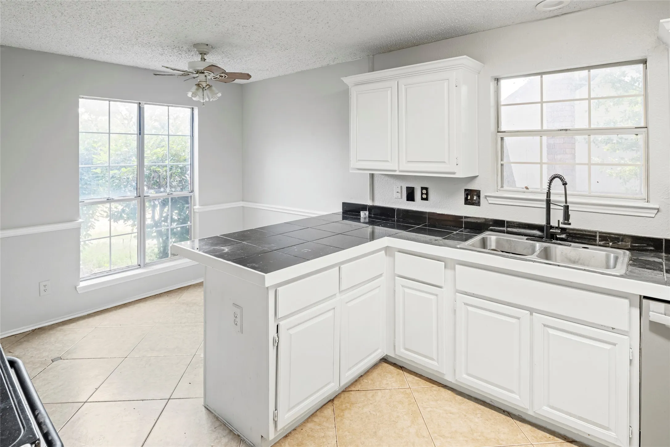 Kitchen featuring white cabinetry, a black tiled countertop, a dual basin stainless steel sink with a black gooseneck faucet, and tile flooring