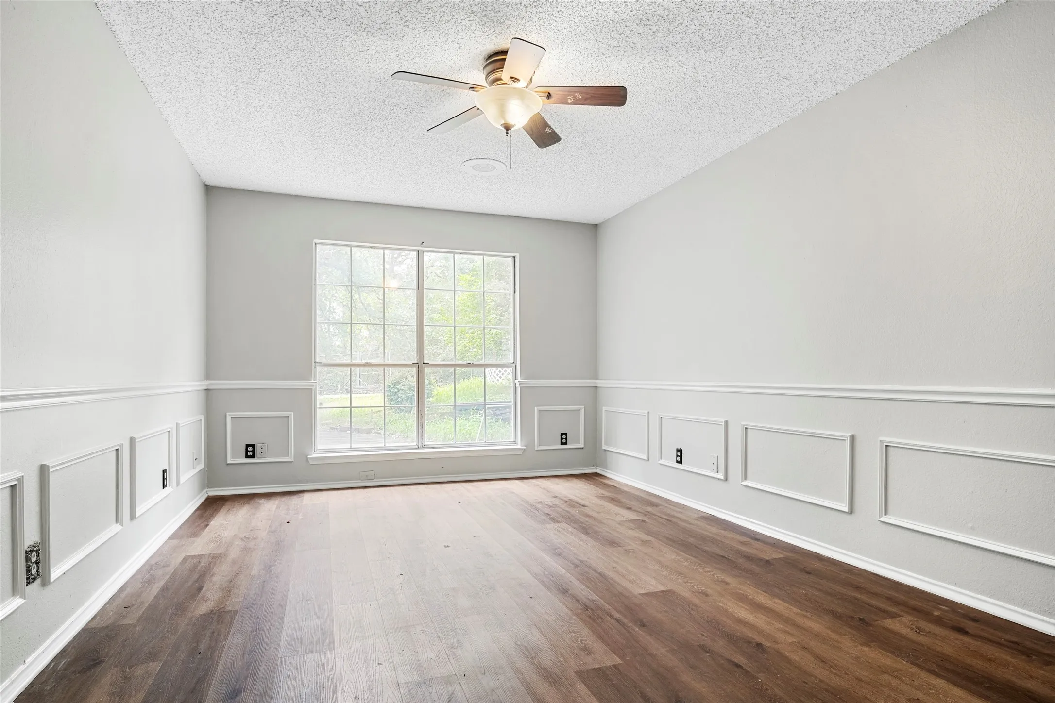 Spacious room featuring wood-finish flooring, a contemporary ceiling fan, and extensive picture frame wainscoting
