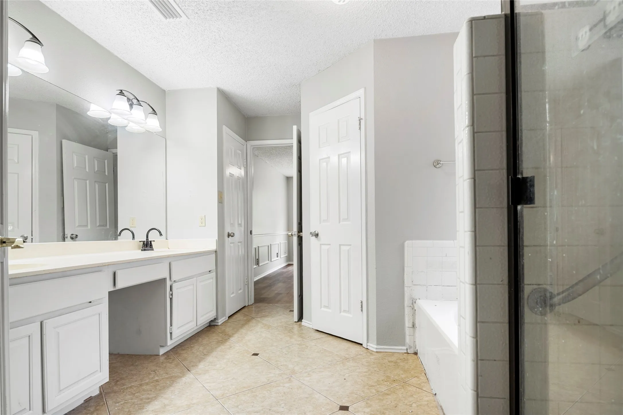 Spacious bathroom featuring a dual vanity with ample counter space, custom cabinetry, tiled flooring, a glass-enclosed shower, and a separate soaking tub