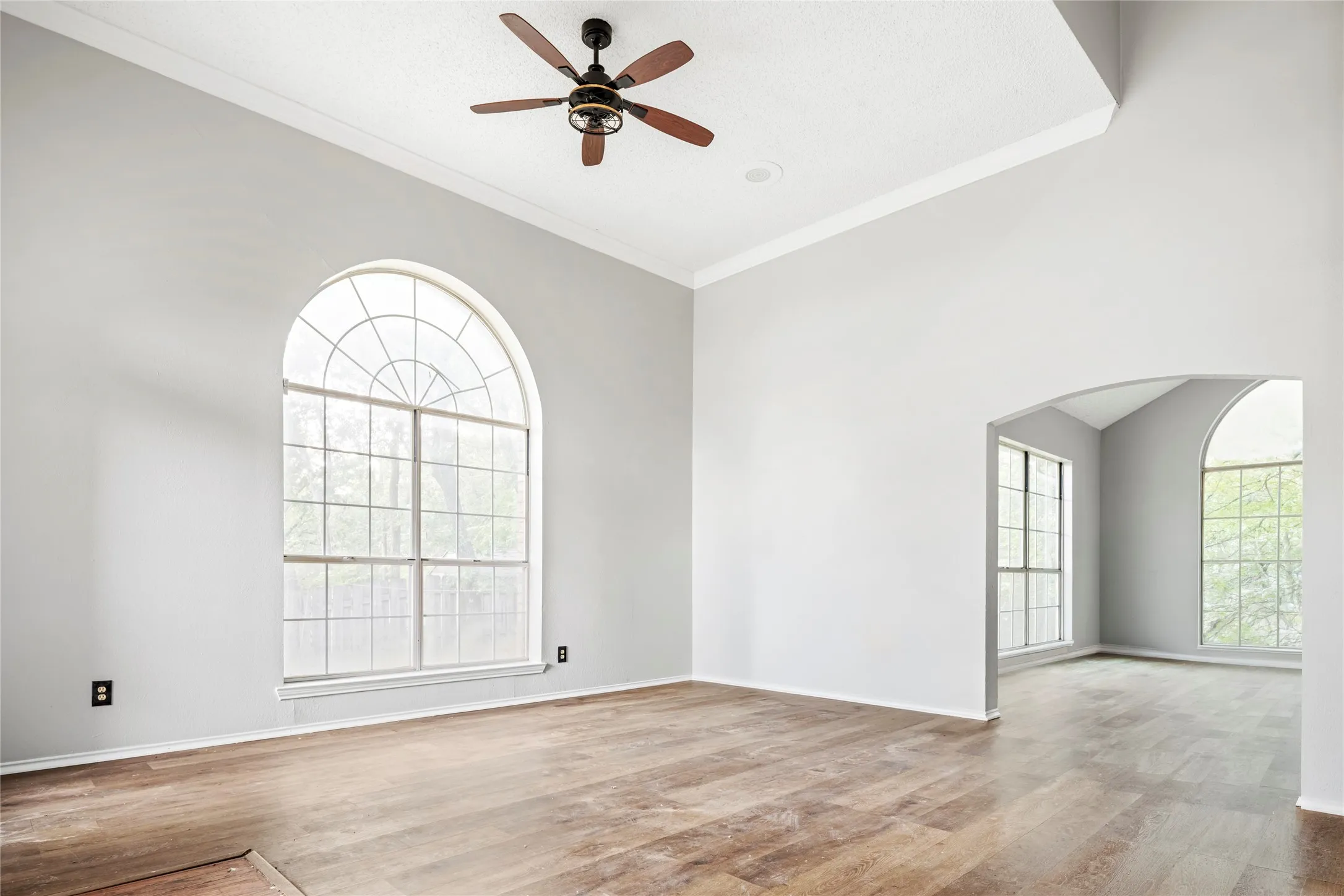 Expansive room featuring a vaulted ceiling with crown molding, a ceiling fan, and wood-finish flooring