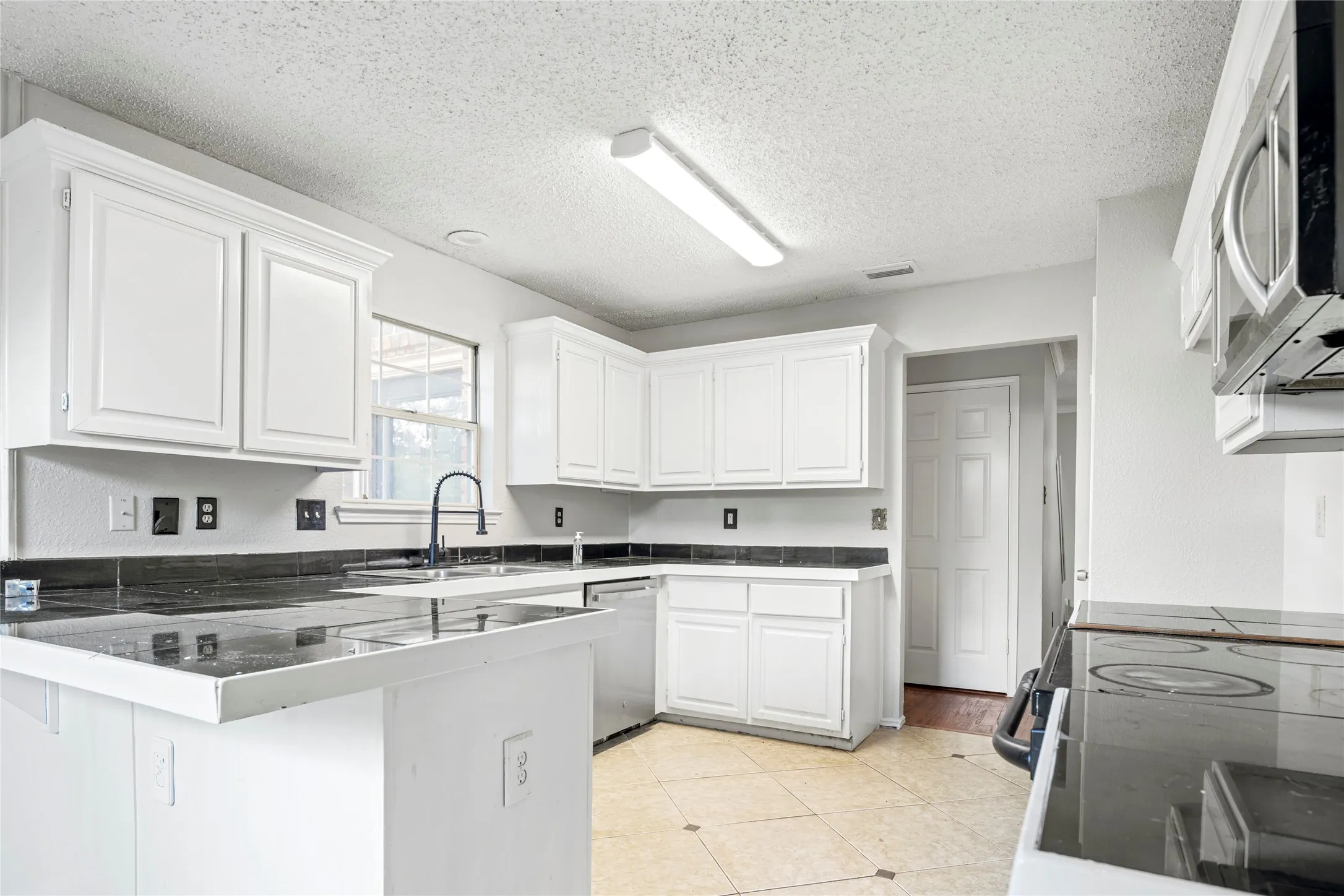Kitchen featuring white cabinetry, dark countertops, tile flooring, a built-in dishwasher, and a microwave oven