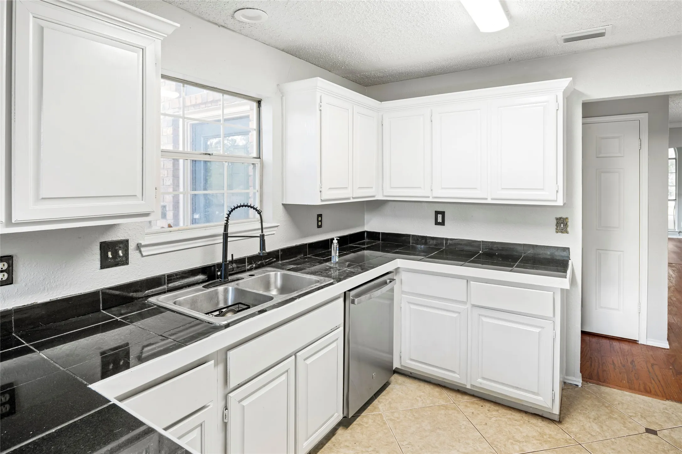 Kitchen featuring white cabinetry, black tile countertops, and a dual basin stainless steel sink with a matte black faucet